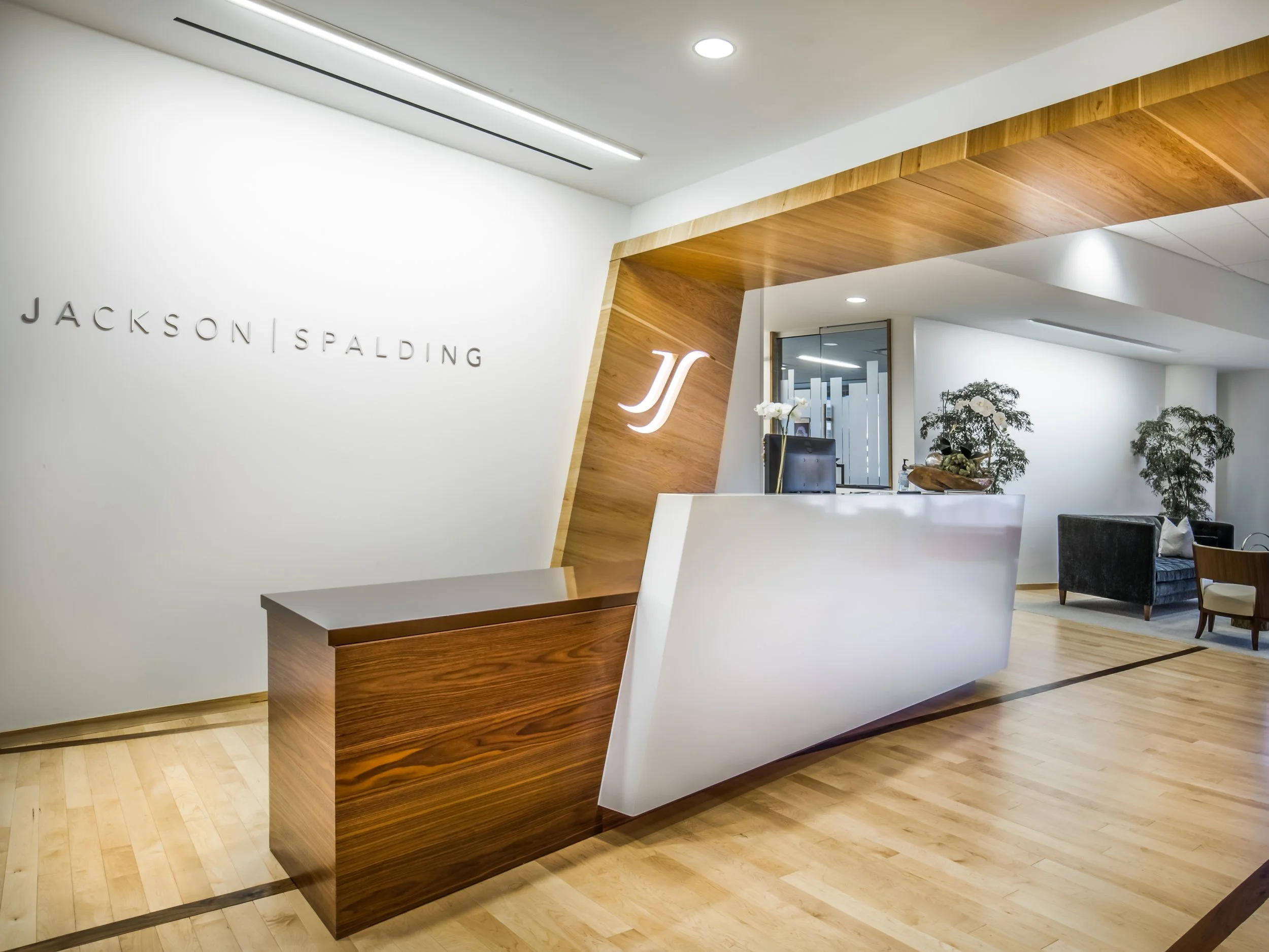 Modern reception area with white walls, wooden accents, and seating including armchairs and side tables, in an office or hotel lobby environment.
