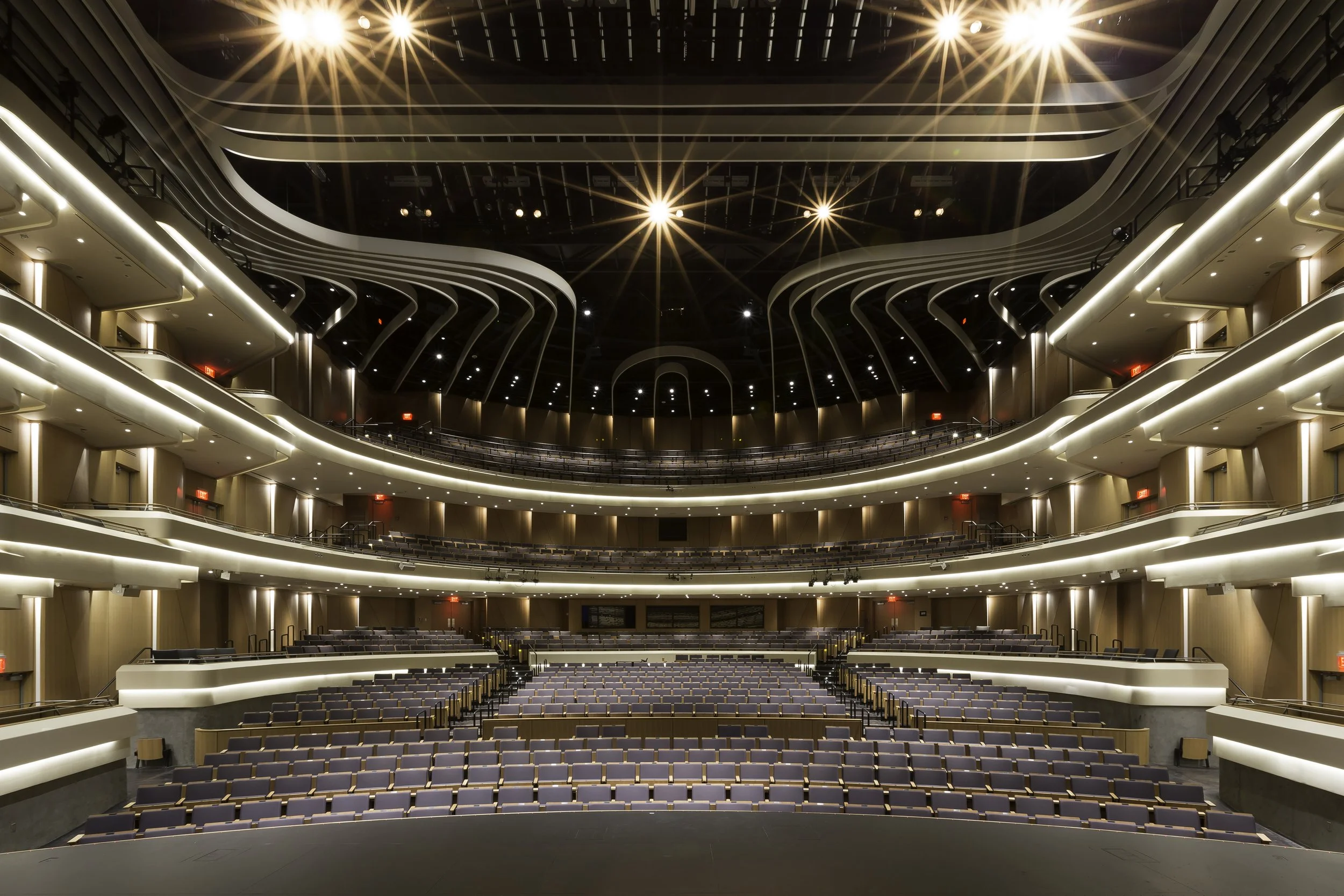 Interior of a modern theater or concert hall with tiered seating, multiple balconies, and bright overhead lighting.