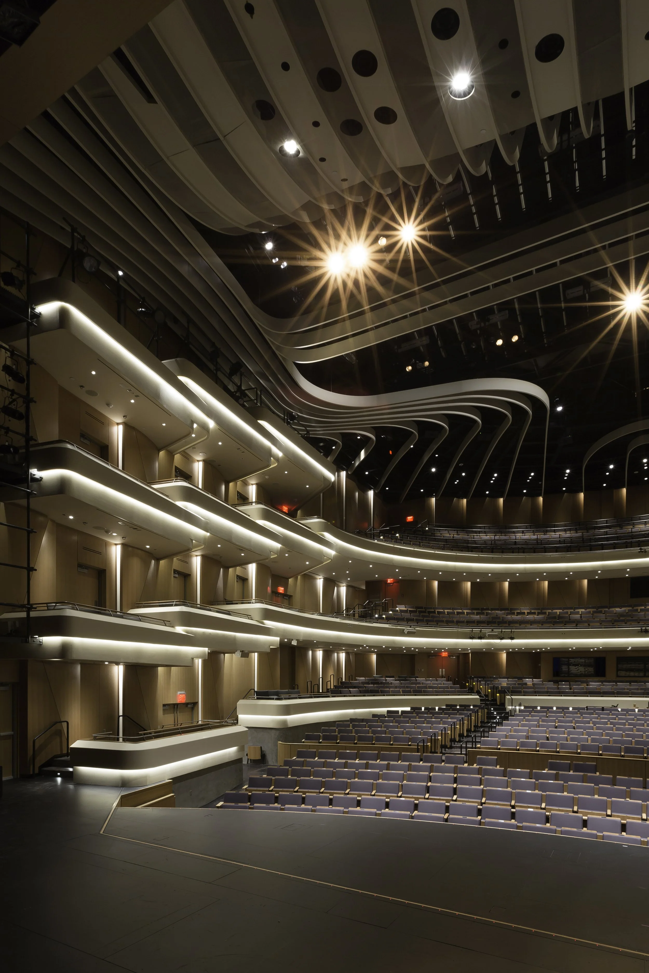 Interior of a modern theater with multiple balconies, wooden walls, and bright overhead lighting.