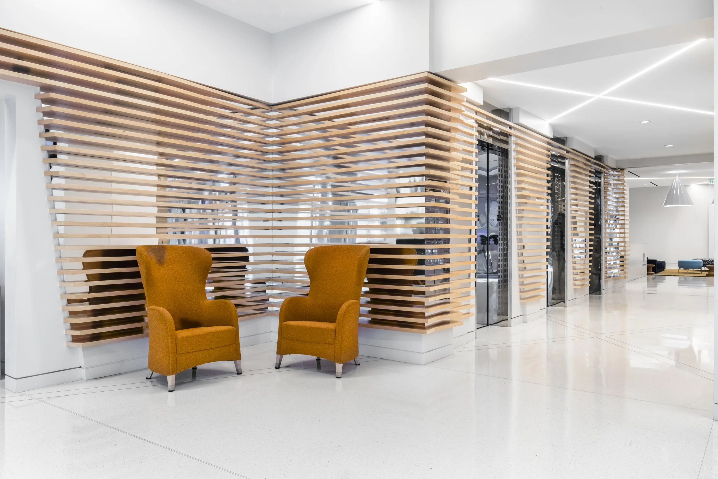 Modern interior space with two mustard yellow high-back armchairs and a wooden slat partition wall.