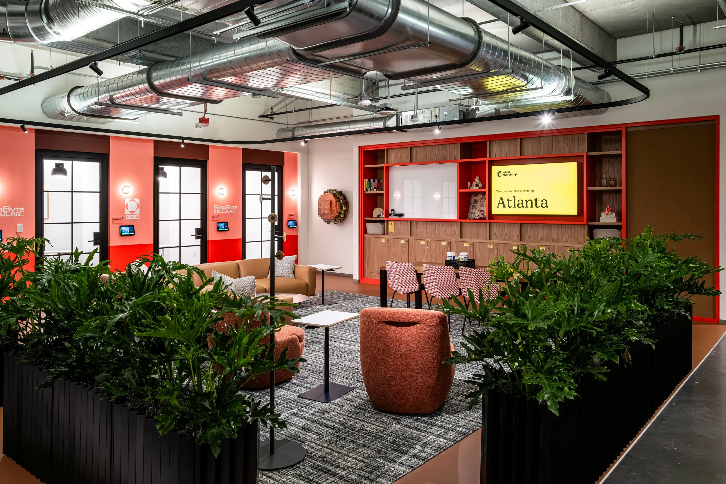 Modern office lounge area with seating, plants, and a large digital screen displaying 'Welcome to Intuit Mailchimp Atlanta'.