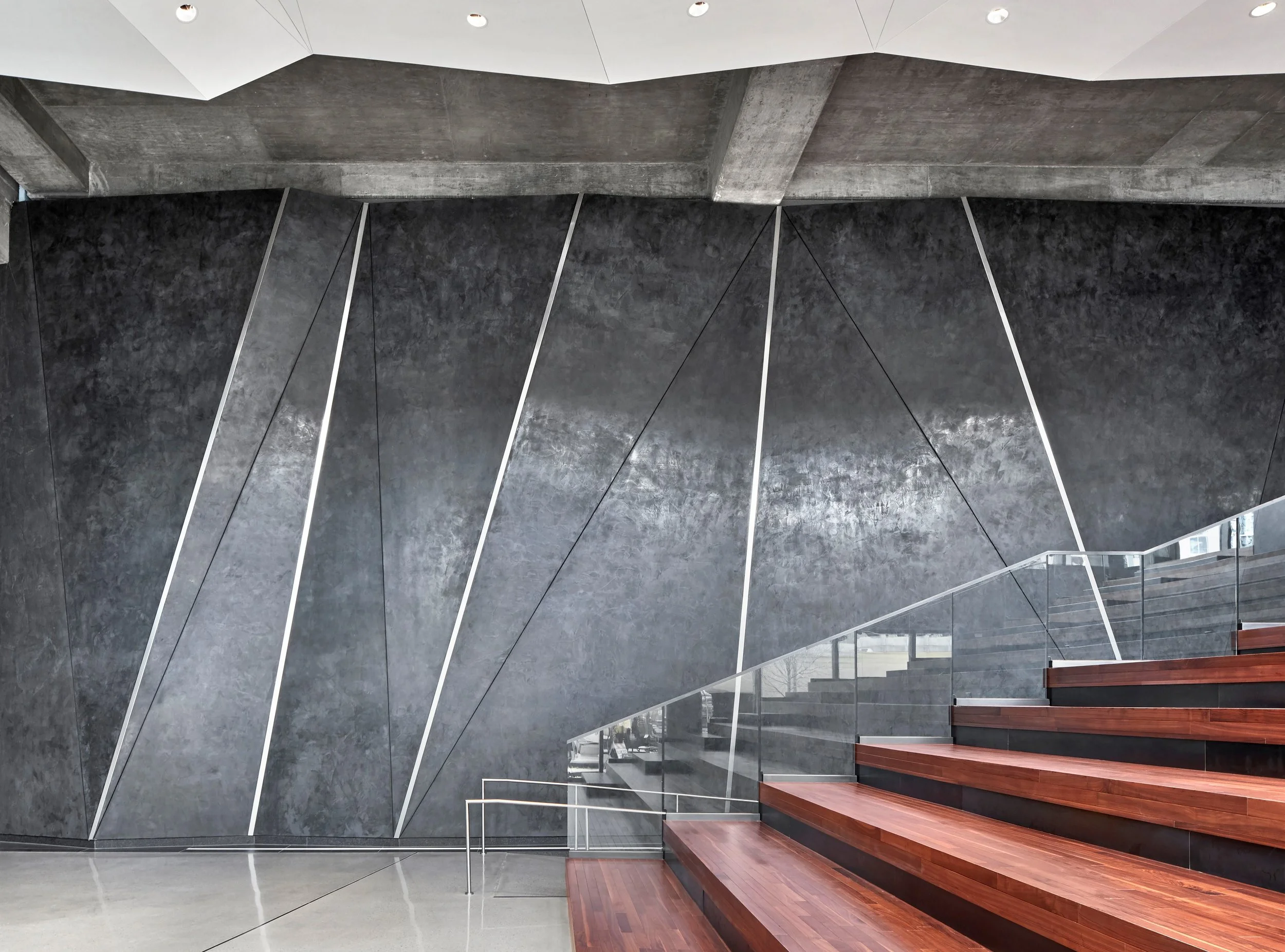 Modern interior with a dark, textured wall featuring geometric lines, glass railing, and wooden stairs.
