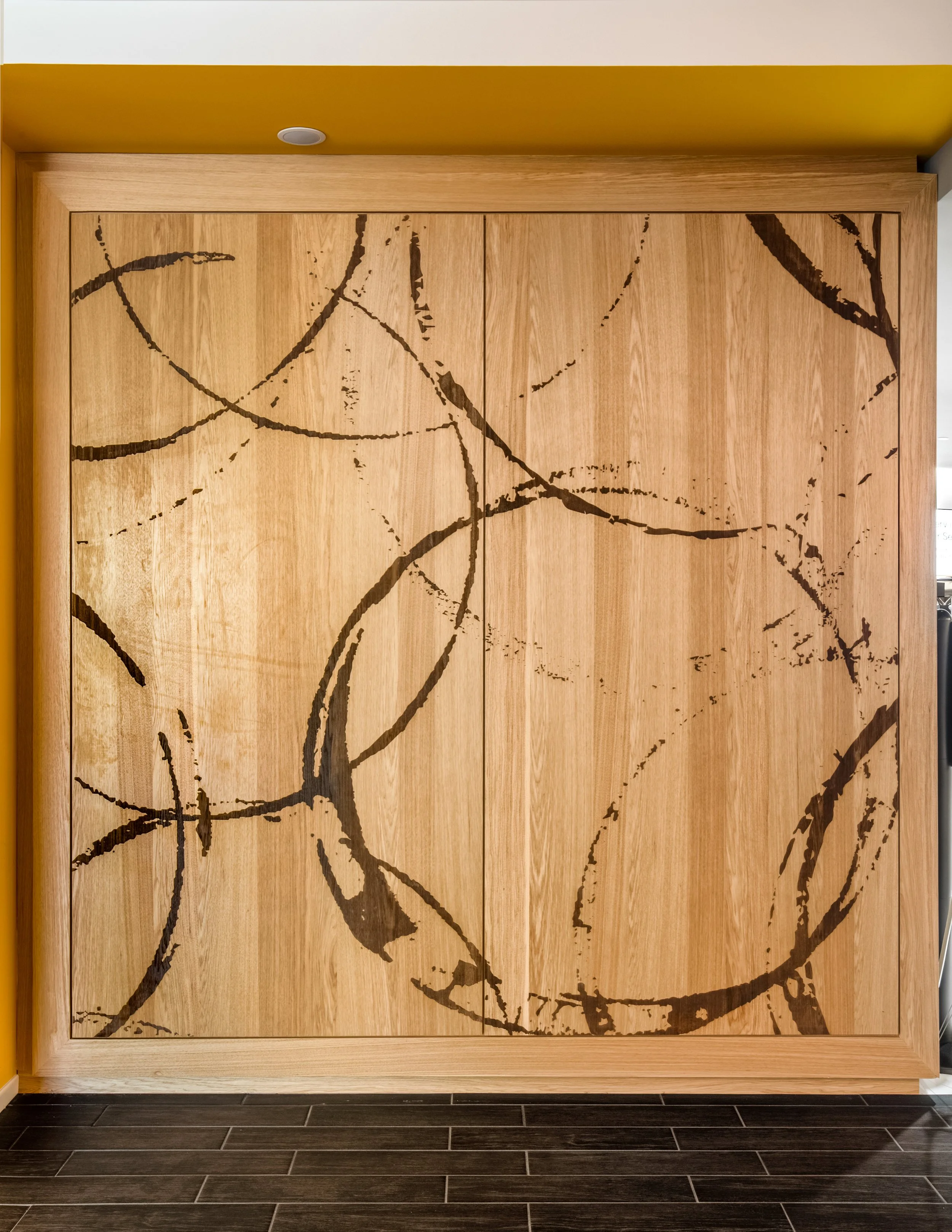 Wooden closet with black abstract line art design on the doors, located next to a yellow wall.
