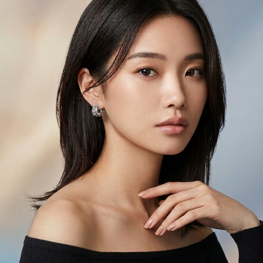 A young woman with shoulder-length dark hair wearing a black off-the-shoulder top and silver earrings, posing against a neutral background.