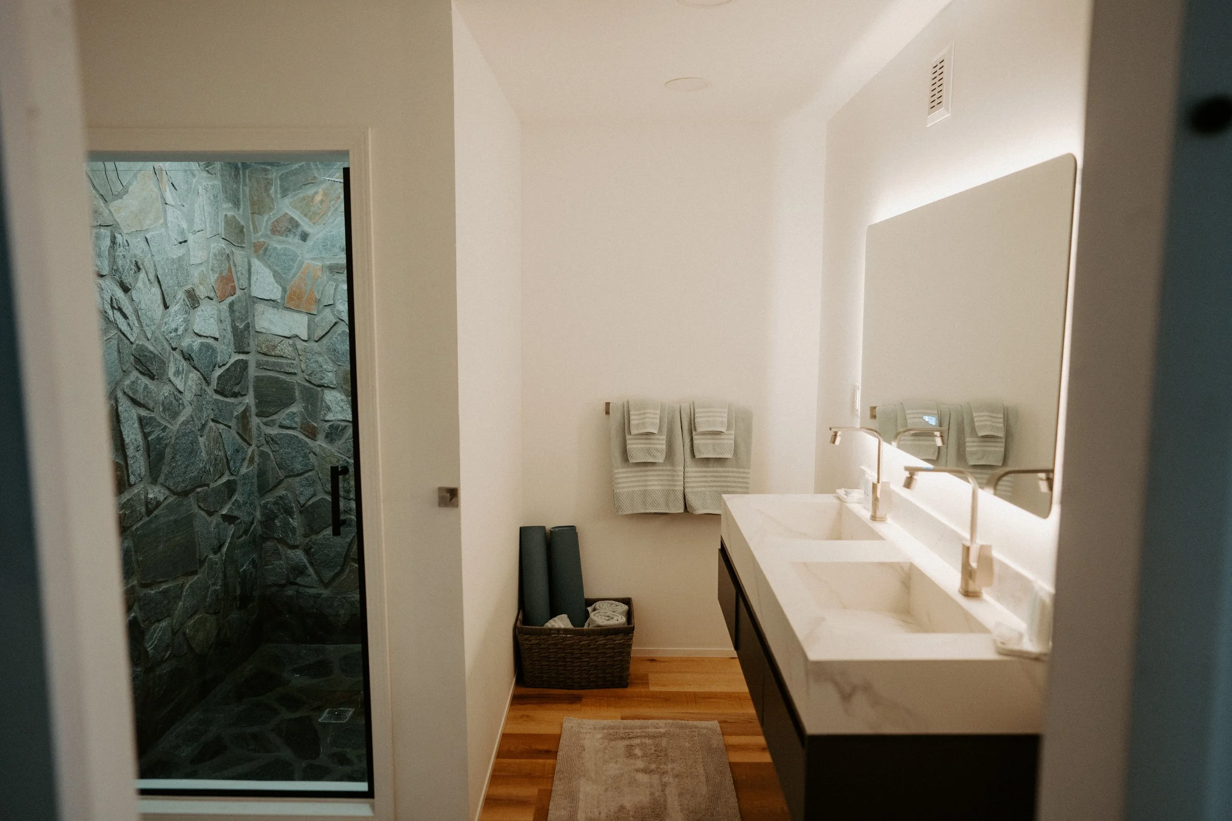 Modern bathroom with double sink vanity, large mirror, and stone shower with a glass door.