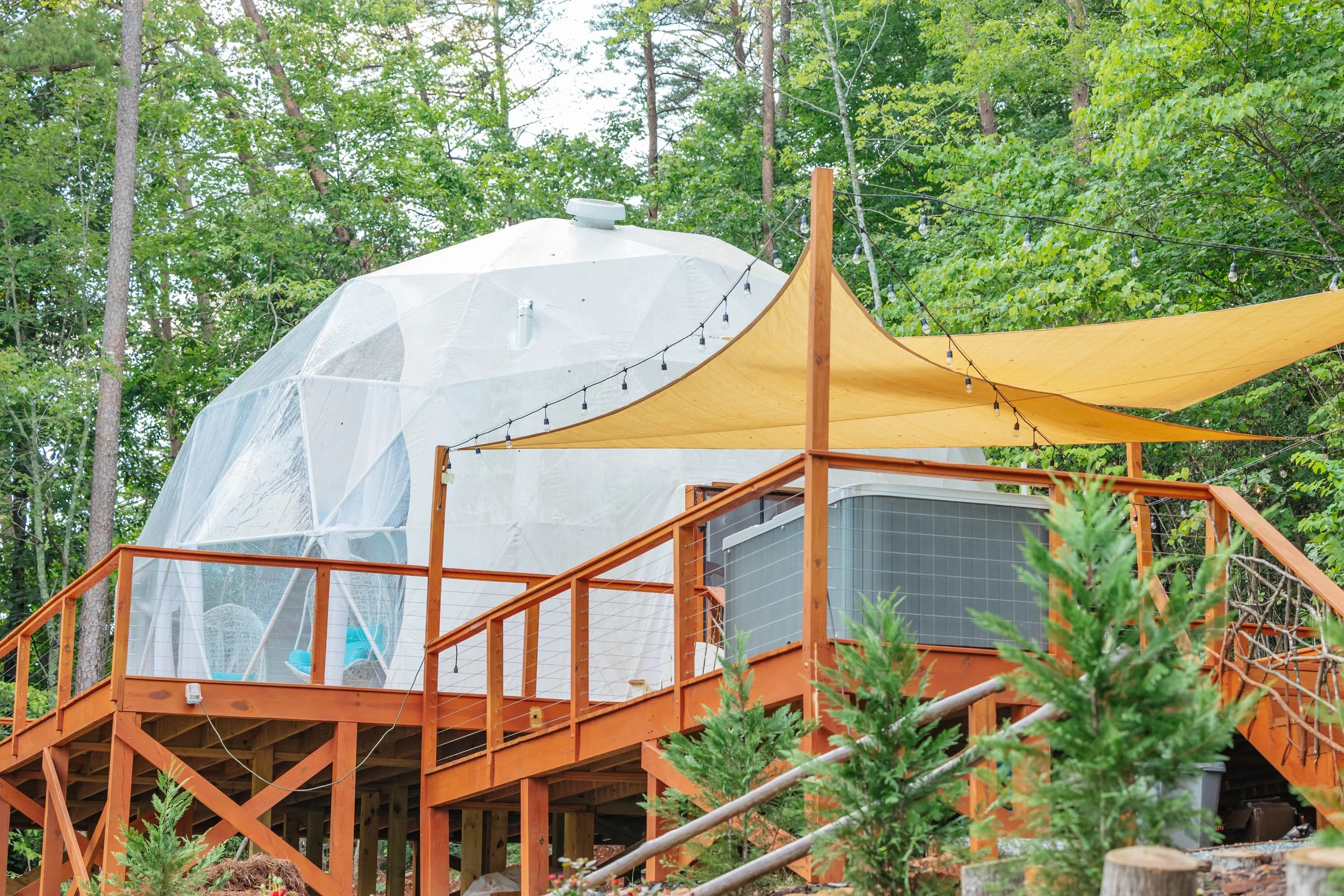 Treehouse with a wooden deck and yellow canopy, surrounded by green trees.
