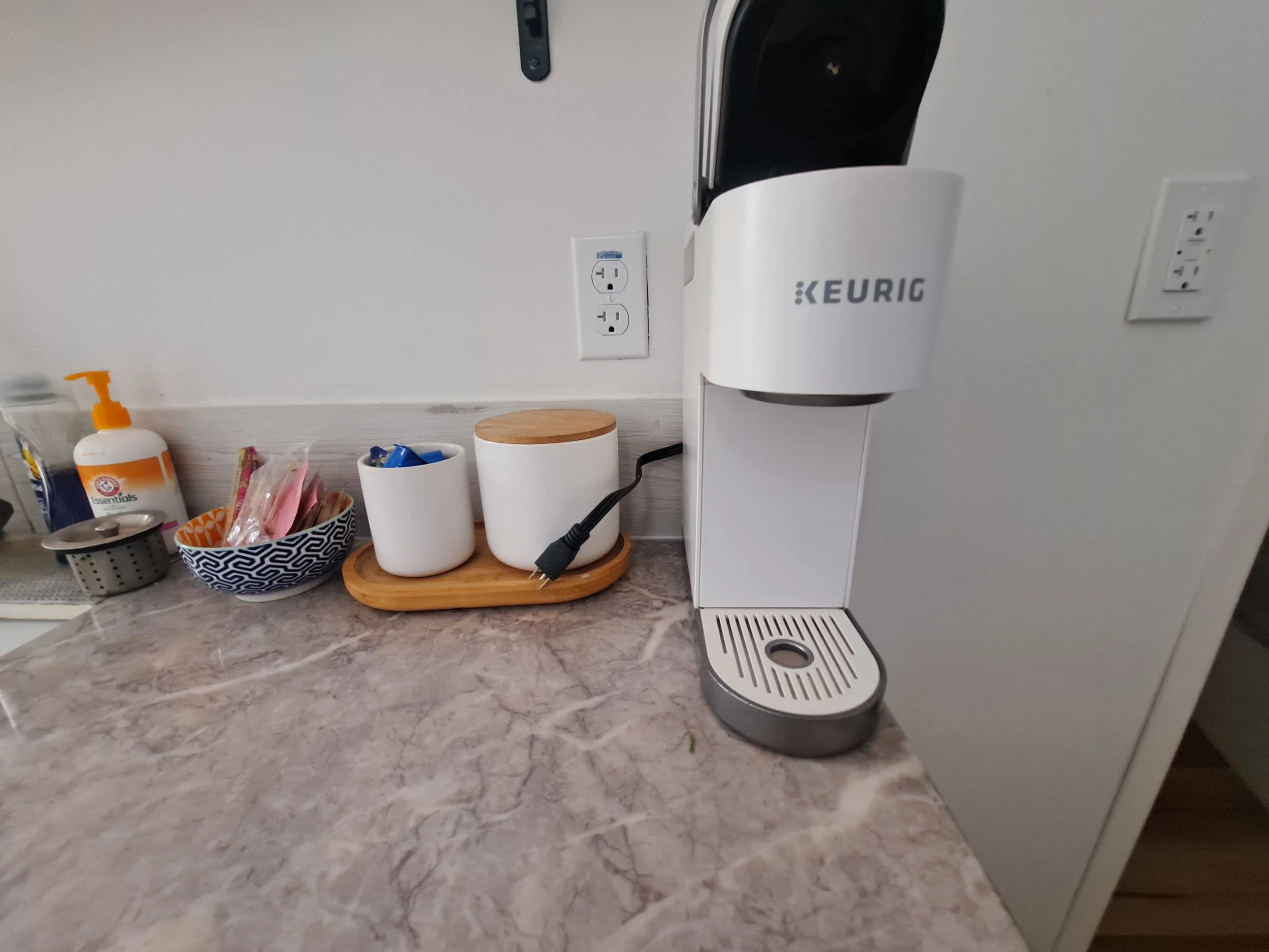 Keurig coffee maker on kitchen countertop with cups, a bowl, and soap dispenser nearby.