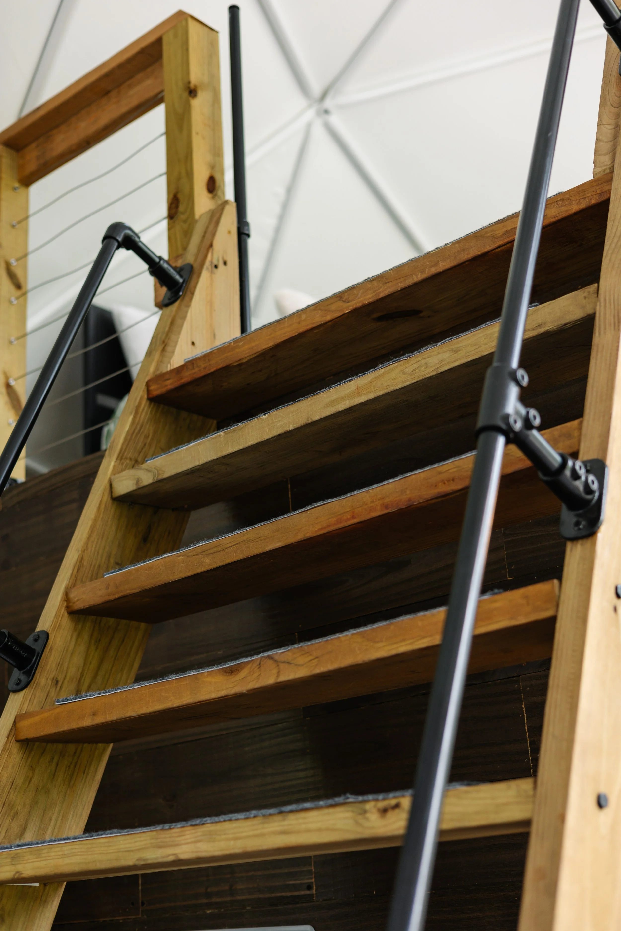 View of a wooden staircase with metal handrails, ascending upward inside a building with a ceiling made of white panels.