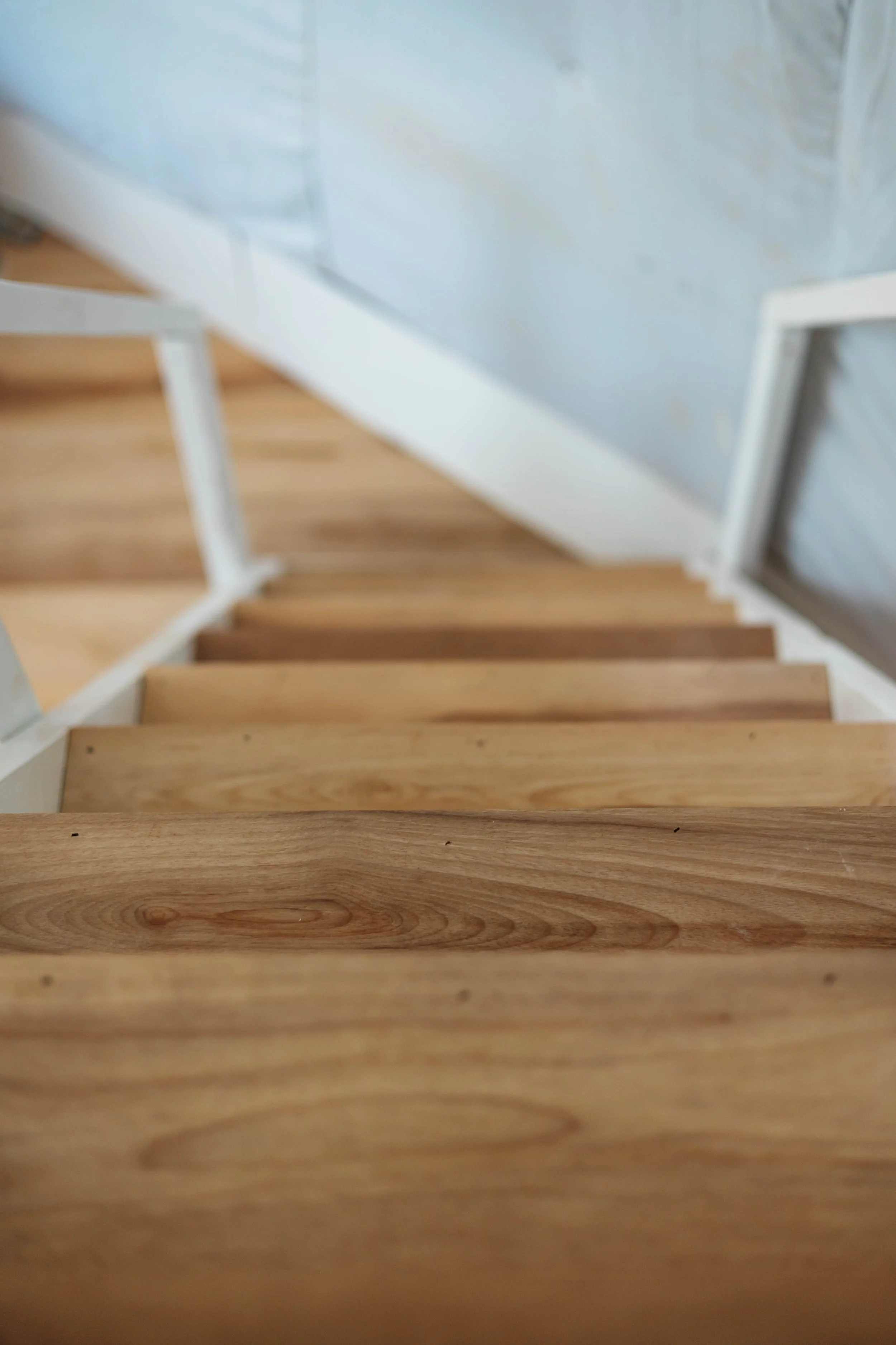 Indoor wooden staircase with white handrails, viewed from the top looking downward.