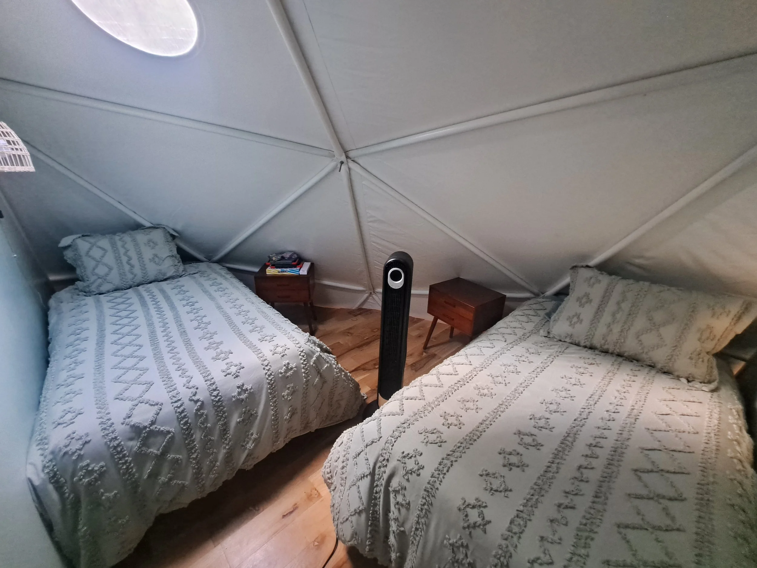 A bedroom with two twin beds covered in white quilted bedspreads, a small nightstand with books in the middle, a fan between the beds, and sloped ceilings.