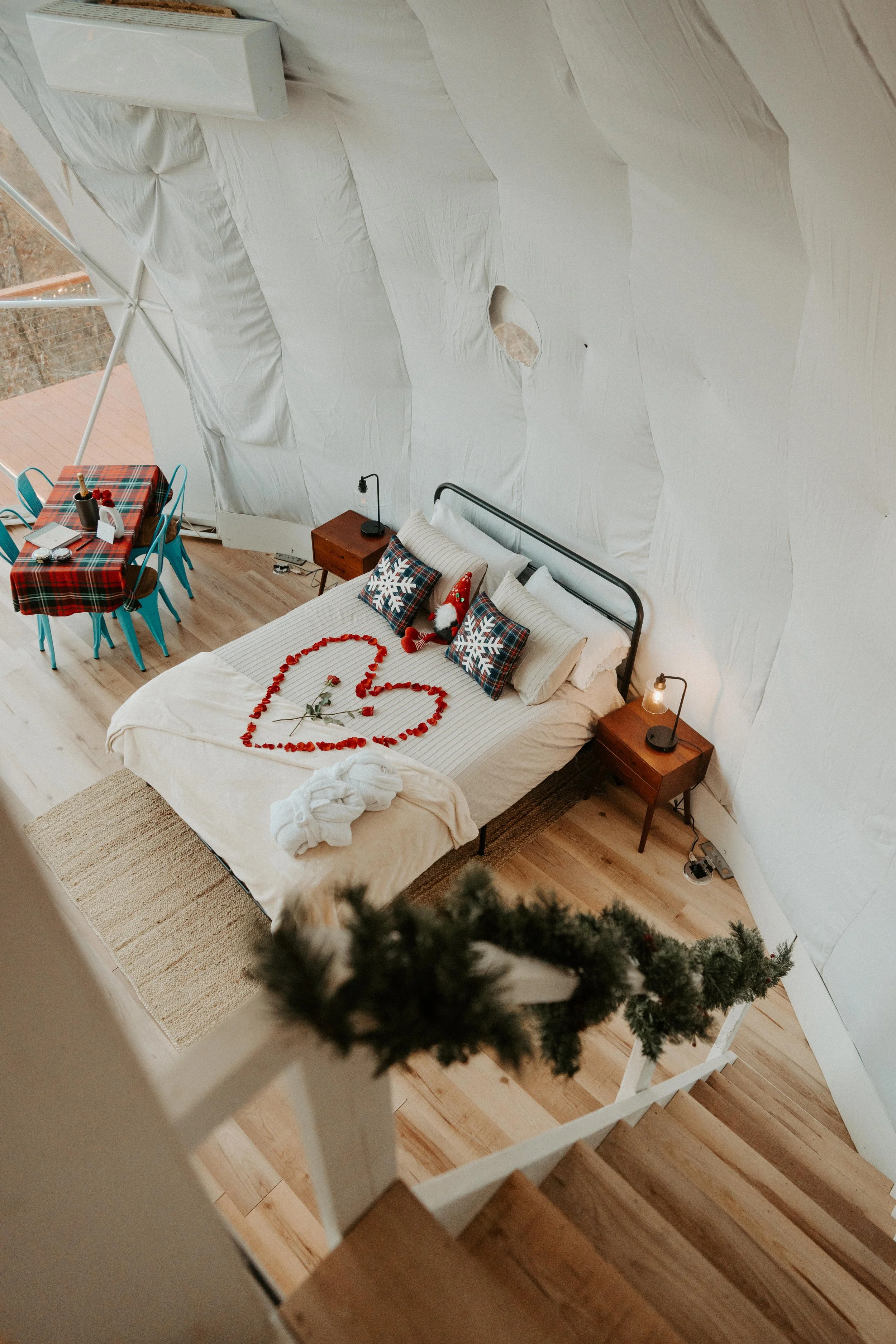 A cozy bedroom decorated for Christmas with red ornaments arranged in a heart shape on the bed, Christmas pillows, and a towel shaped like a bird.