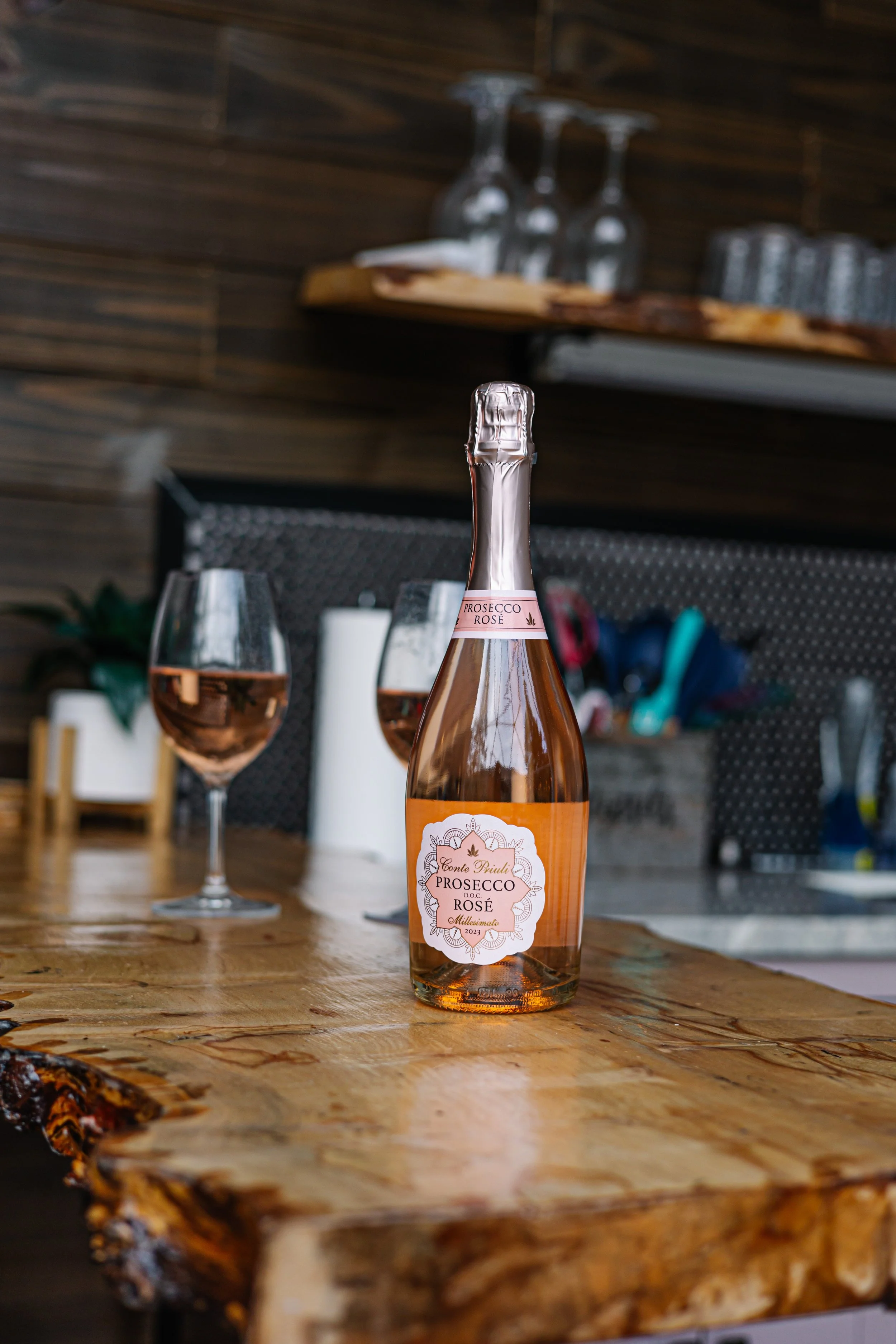A bottle of Prosecco Rosé with two glasses filled with rosé wine on a rustic wooden table.