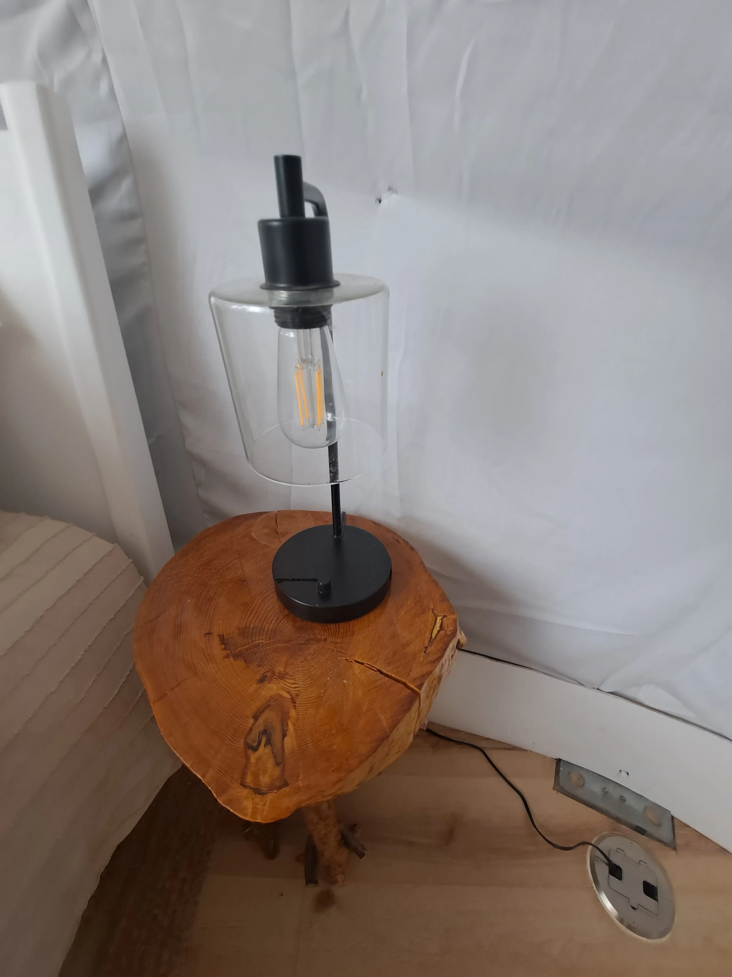 Modern table lamp with black metal stand and clear glass shade, placed on a natural wood side table in a cozy room.
