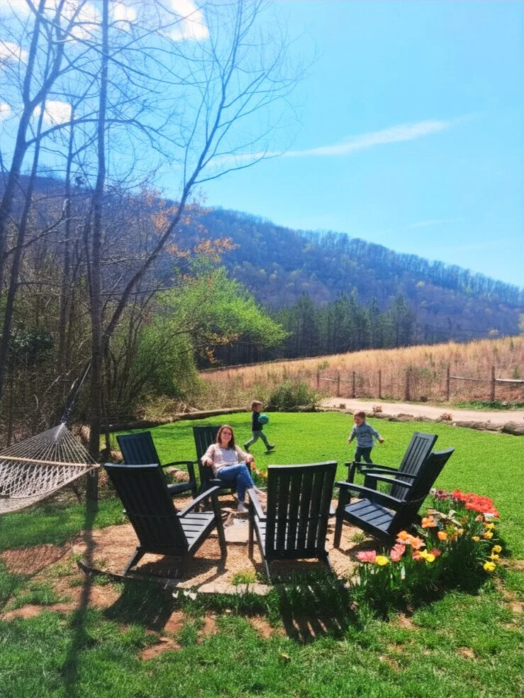 Family relaxing outdoors at Carolina Domes in Union Mills, North Carolina, with children playing on the lawn and Blue Ridge Mountain views in the background.