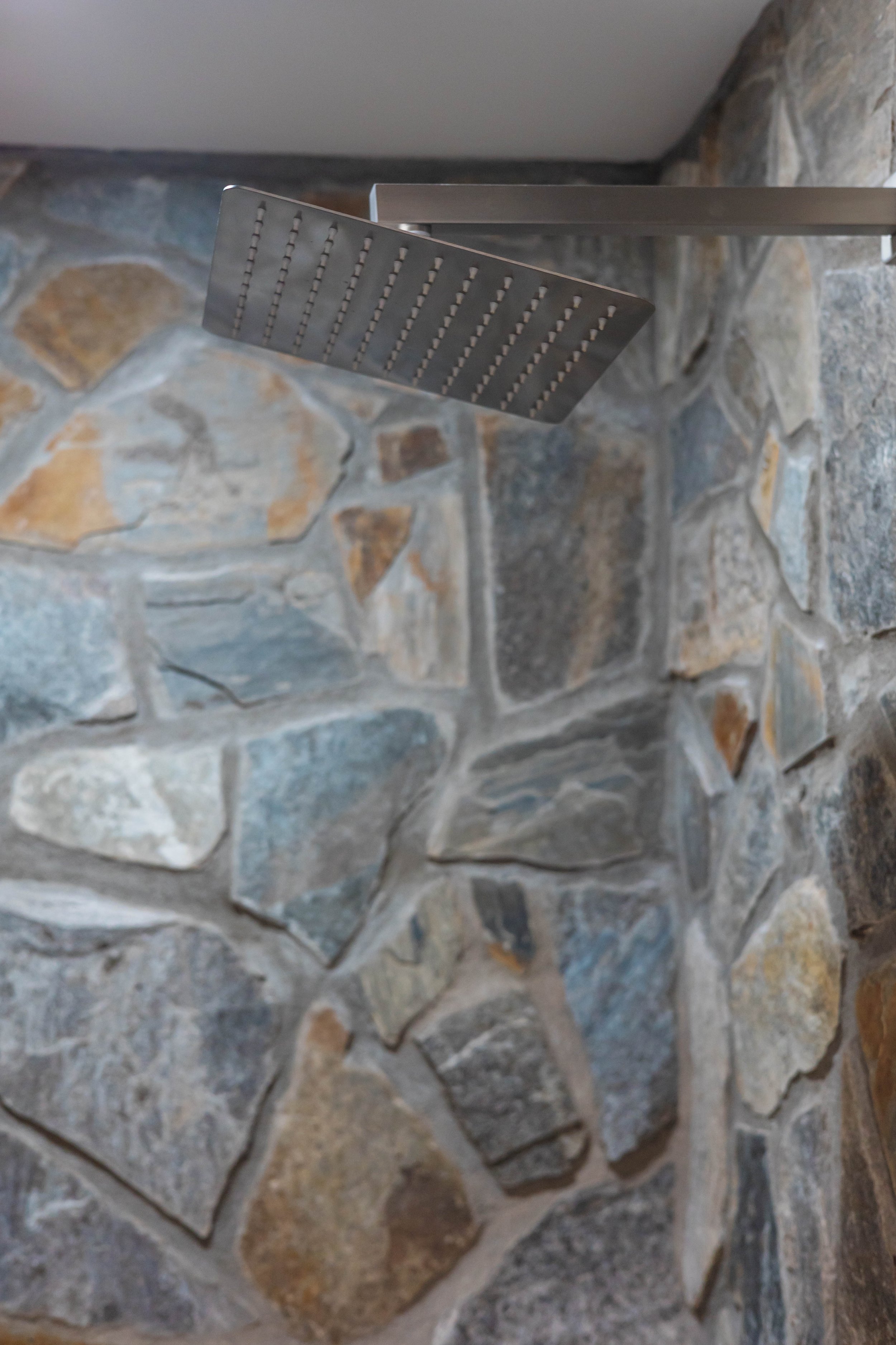 Close-up of a modern shower head mounted on a stone wall in a bathroom.