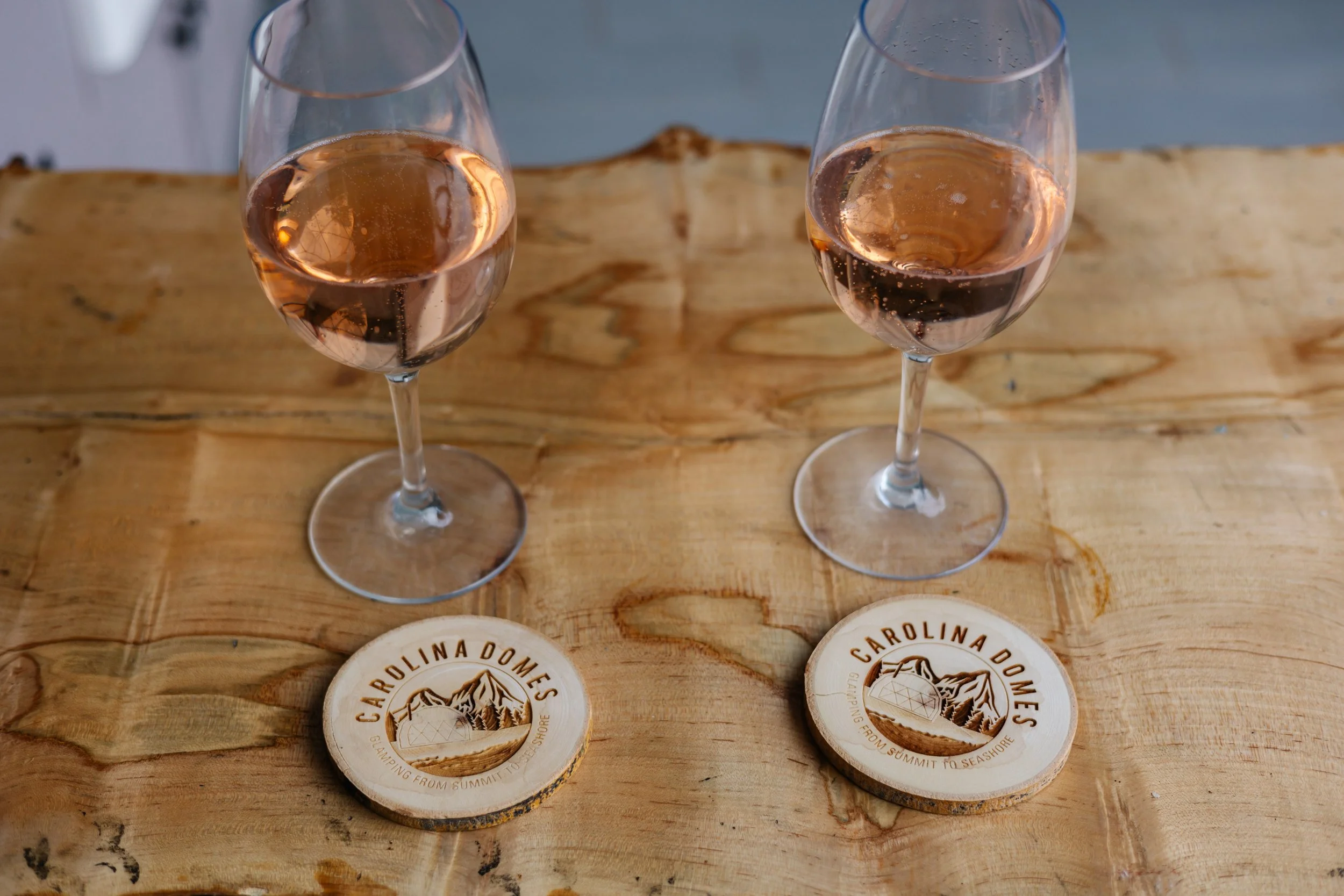 Two glasses of rosé wine on a wooden surface with Carolina Dunes coasters.