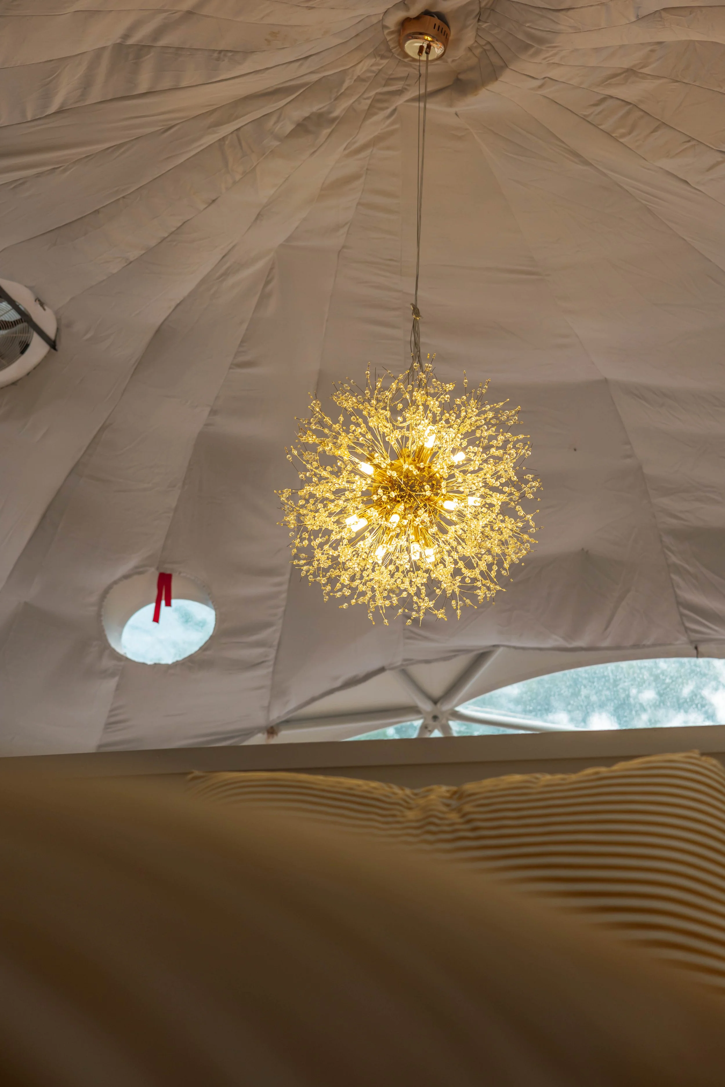 A gold chandelier with crystal-like branches hanging from a ceiling with draped white fabric.