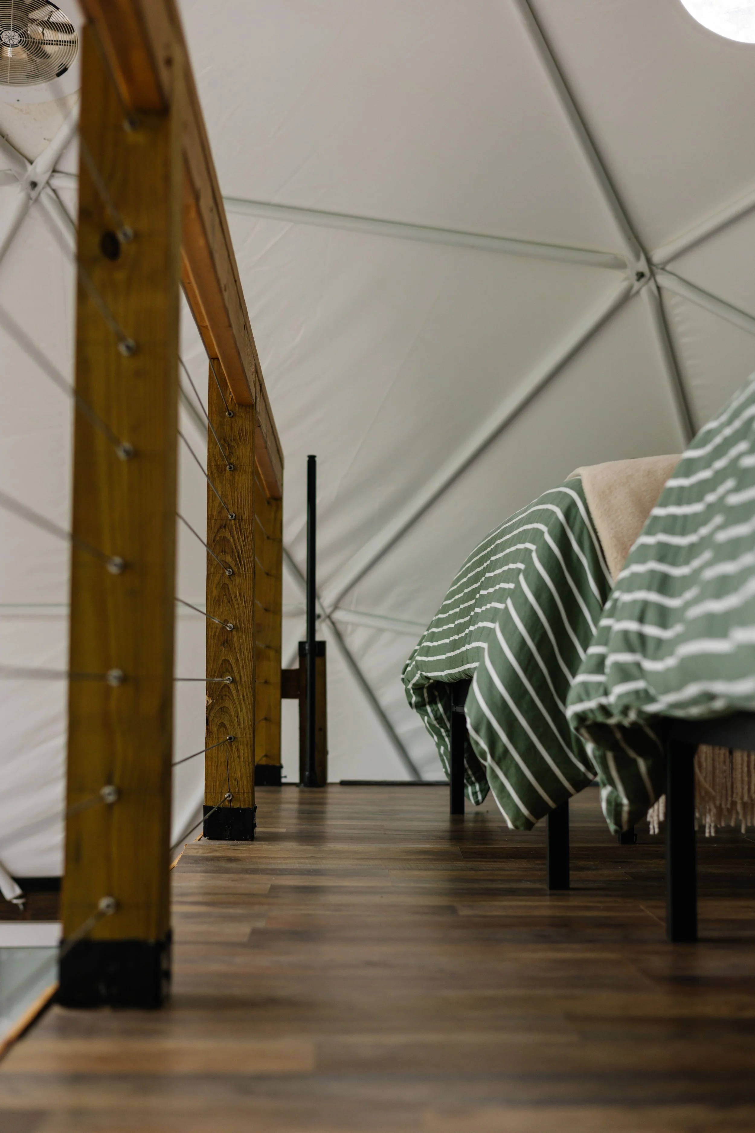 Low-angle view of a cozy indoor space with wooden and metal furniture, striped green and white bed covers, and a white ceiling with geometric patterns.