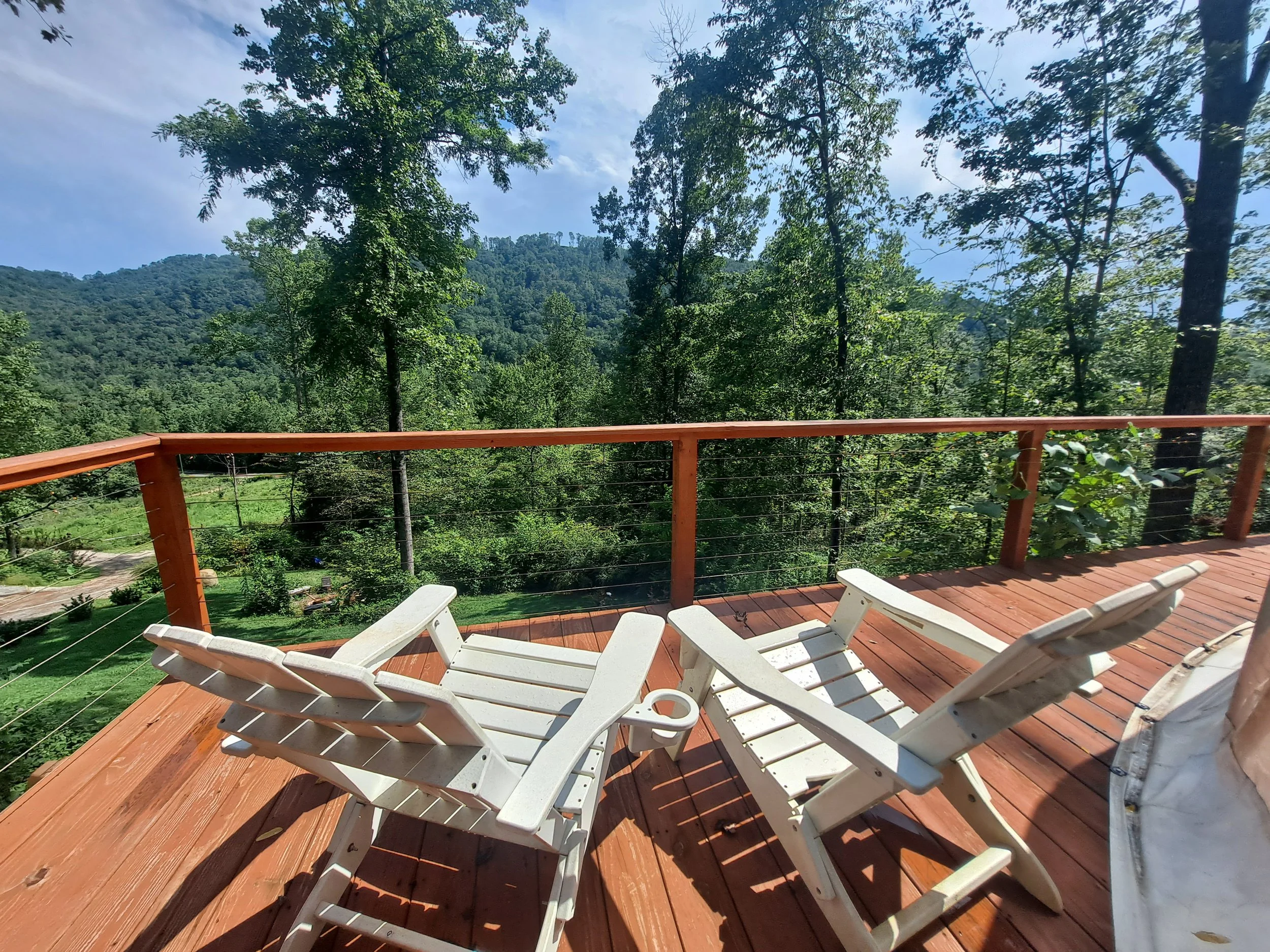 Two white lounge chairs on a wooden deck with a view of green trees and mountains in the distance.