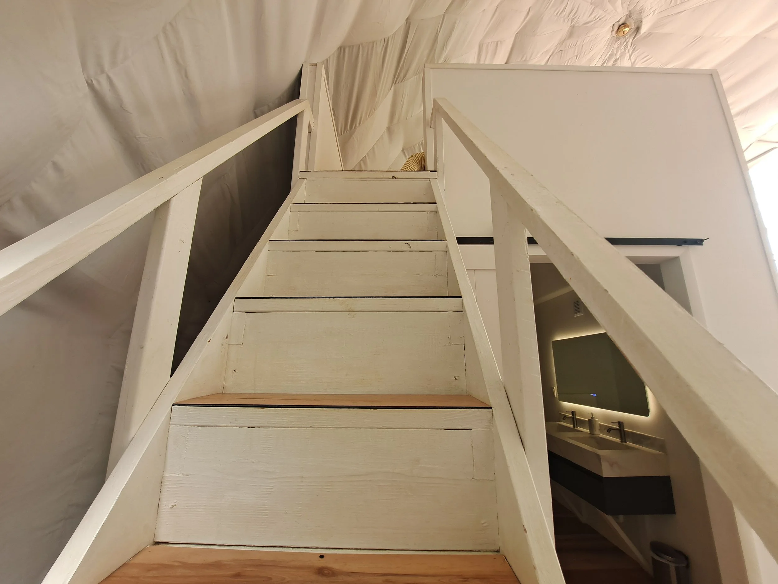 White wooden staircase leading up to a loft area with a railing, located inside a tiny home or similar space.