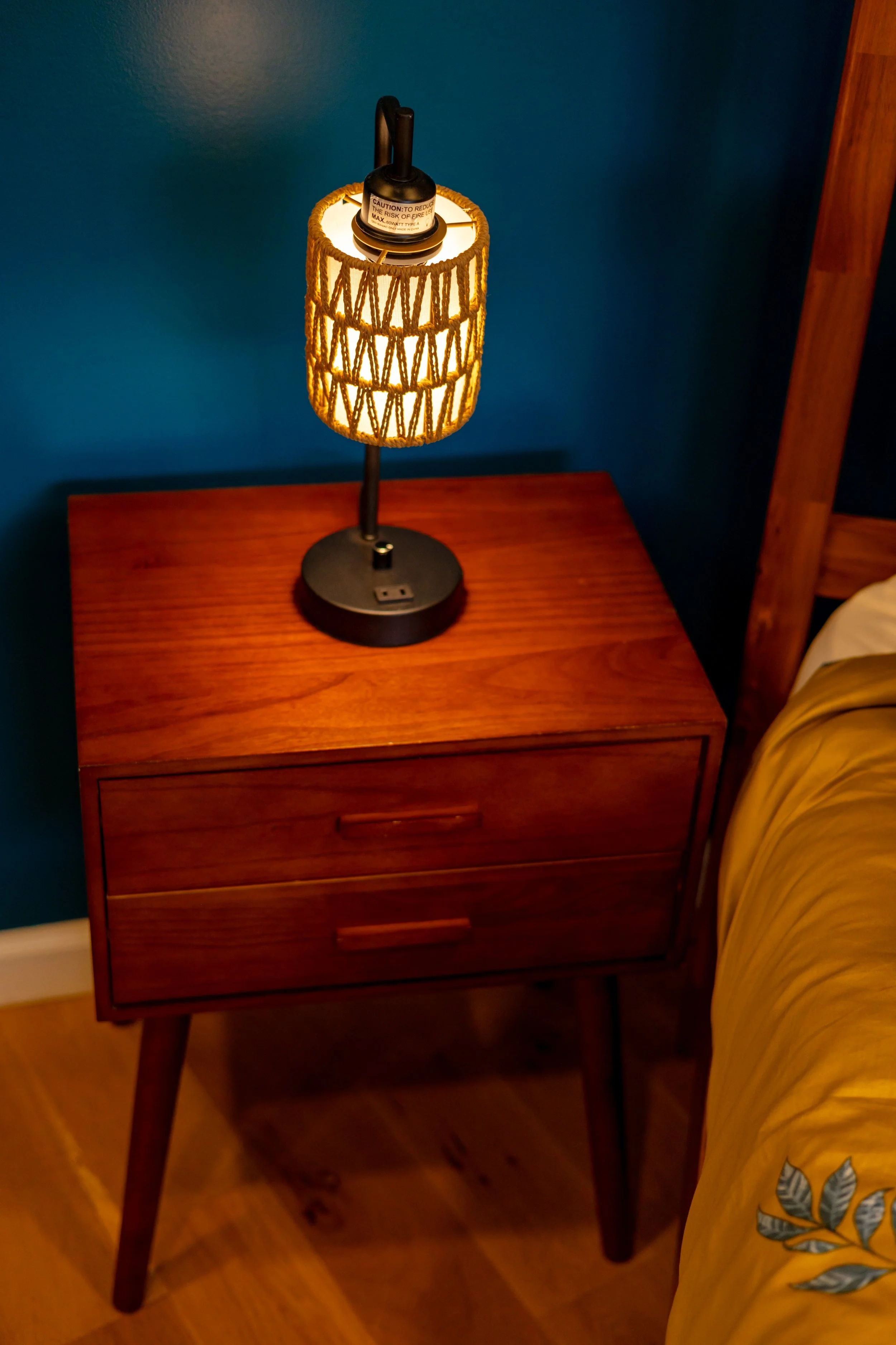 A bedside wooden nightstand with a lamp on top, against a blue wall.