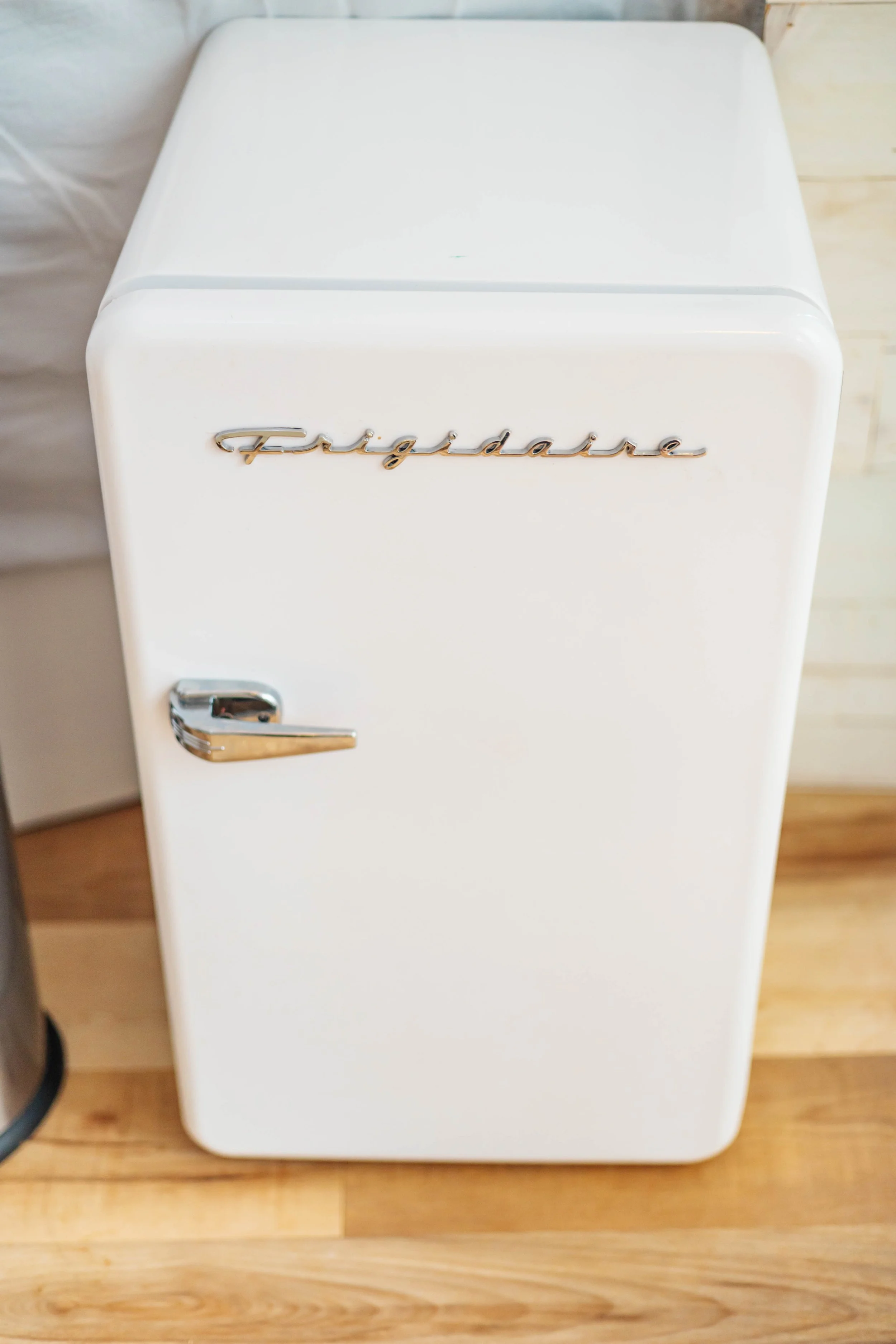 A vintage white refrigerator with chrome accents and a cursive logo reading 'Frigidaire' on the door, placed on a wooden floor.