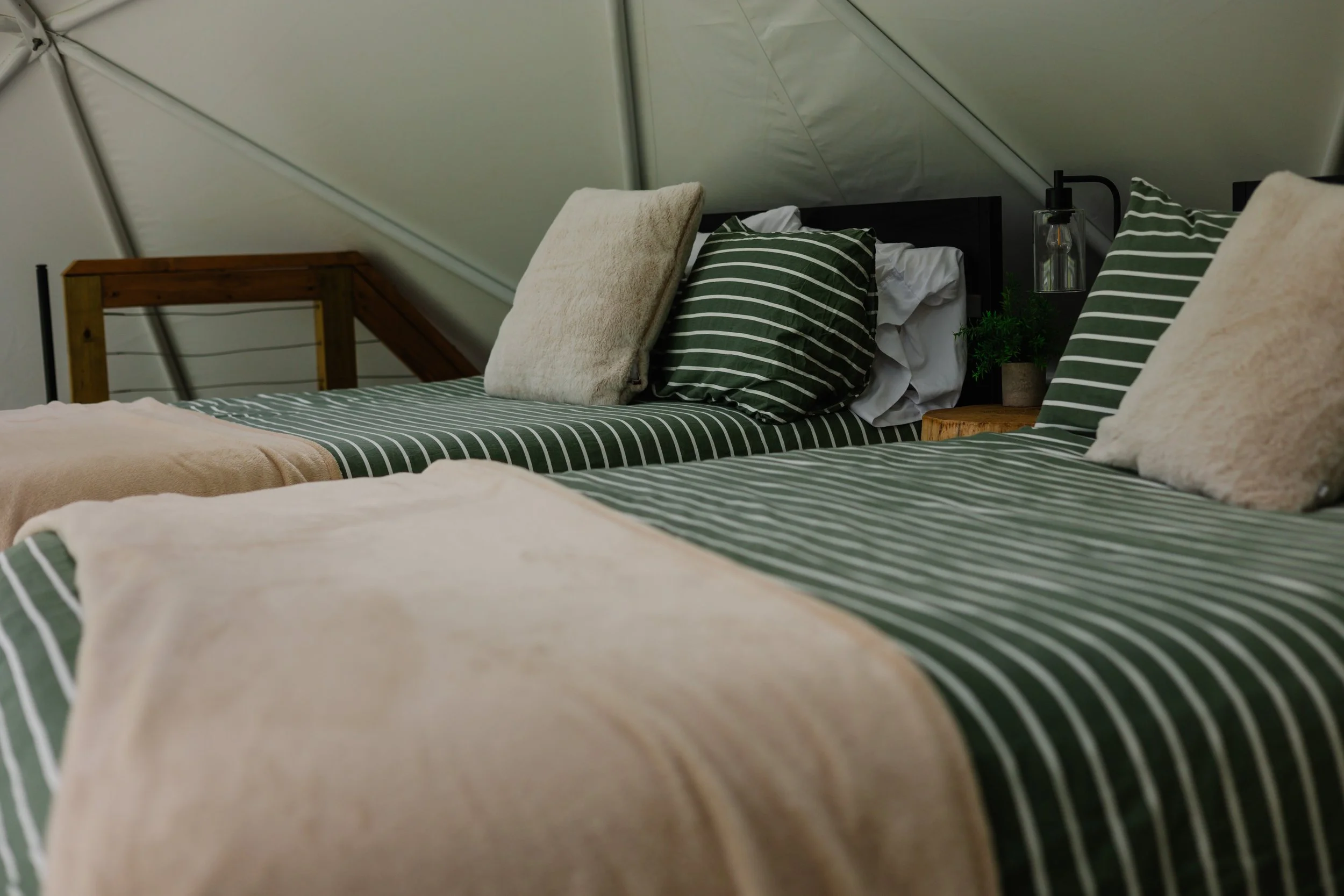 Two beds with green and white striped bedding, beige blankets, and fluffy pillows in a cozy room with sloped ceiling and wooden furniture.