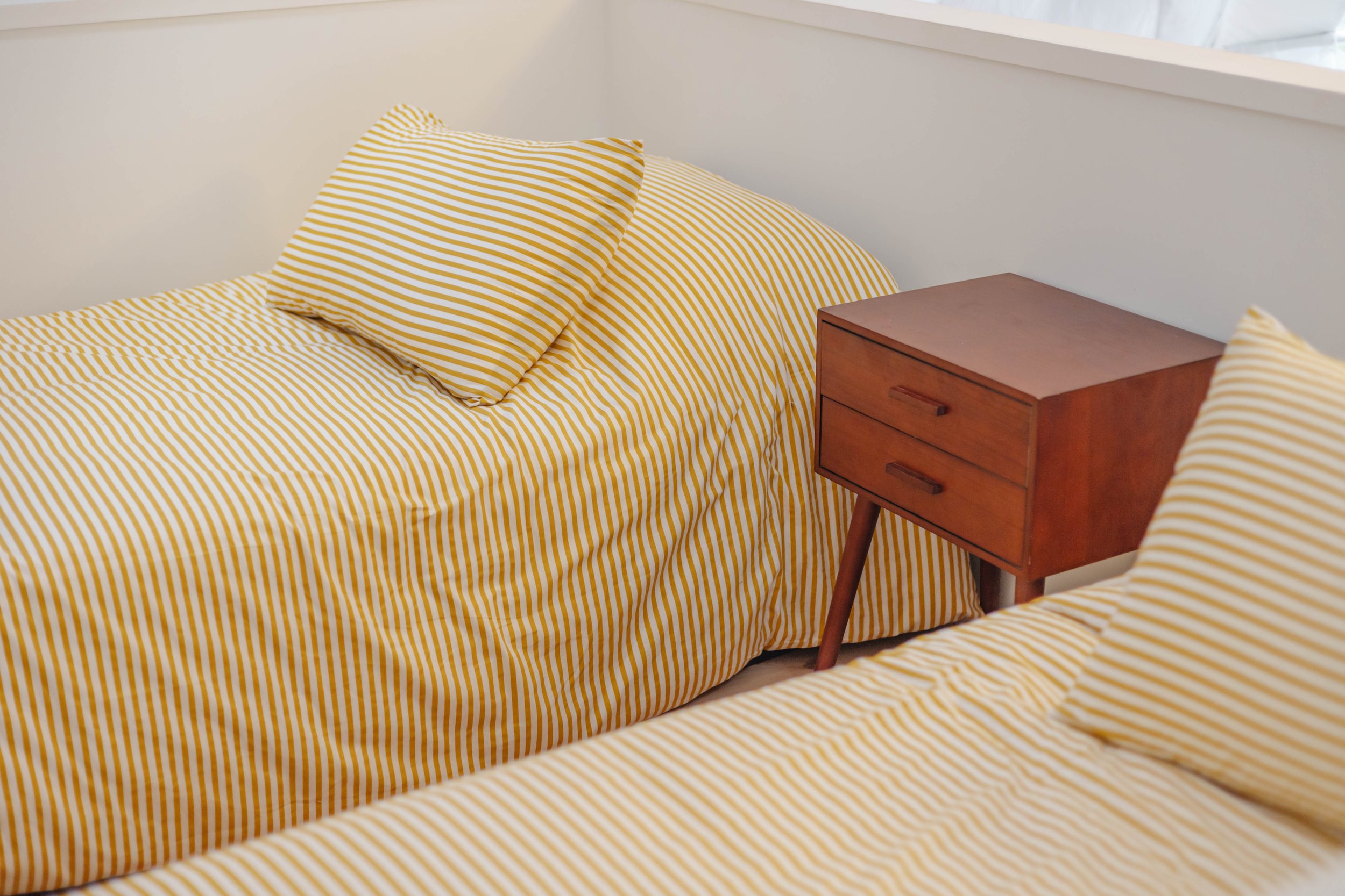 Two beds with yellow and white striped bedding and pillows, and a wooden bedside table between them.