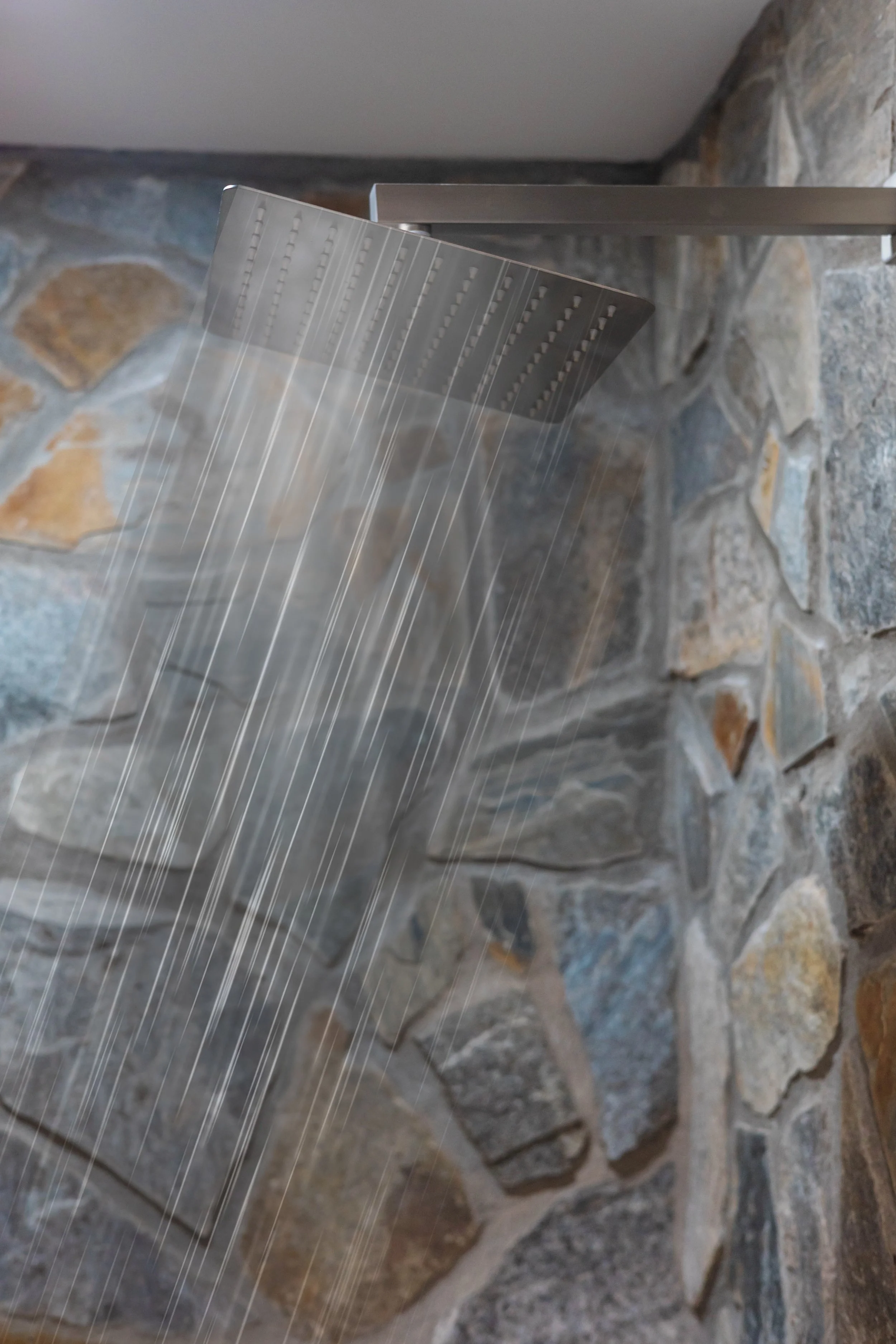 Modern showerhead with water streams against a stone wall background.