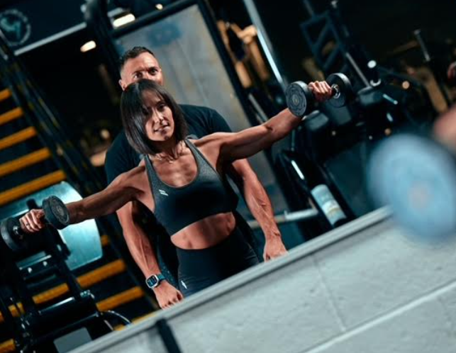 Empty gym with weightlifting equipment and running mats, illuminated by track lighting.