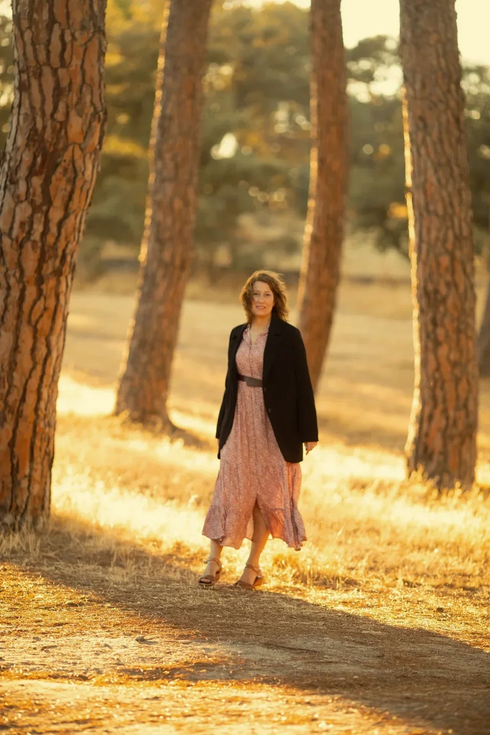Mujer caminando en un bosque con árboles altos durante el atardecer, con luz dorada