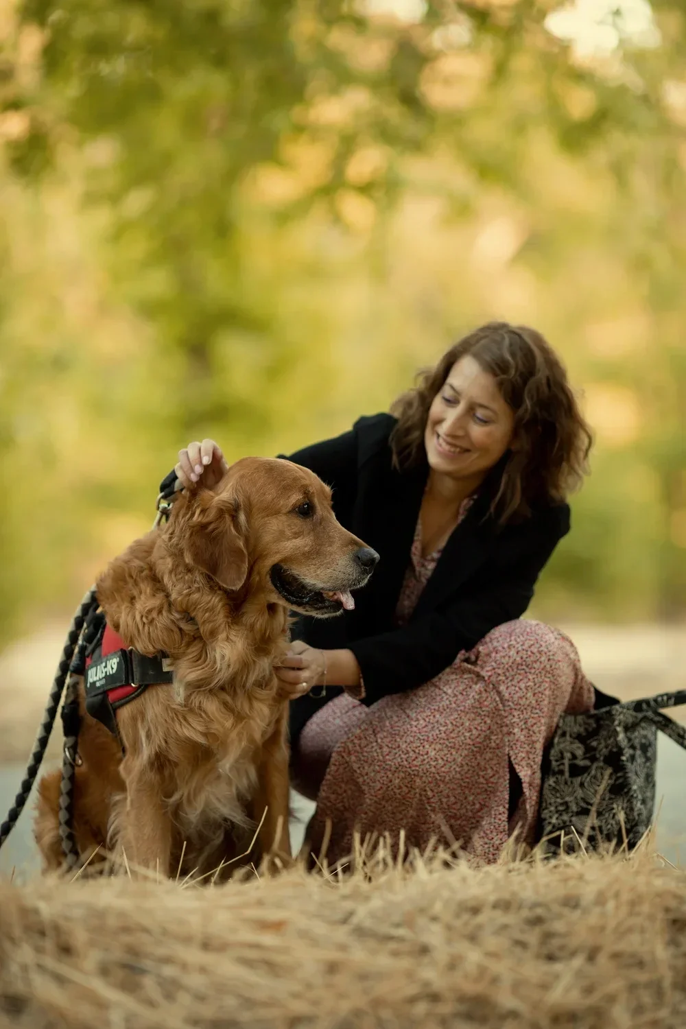 Mujer sonriendo con su perro golden retriever en un parque con fondo de árboles en otoño.