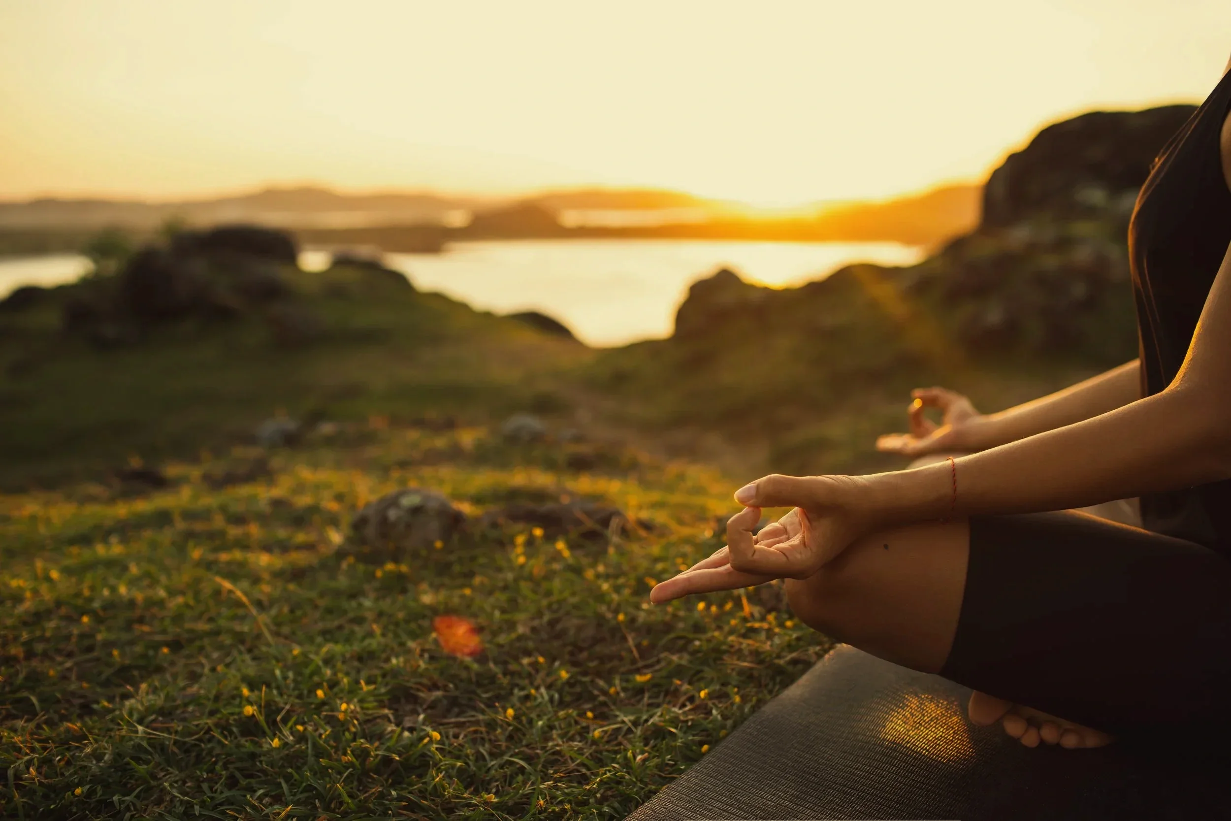 Personas practicando yoga en la naturaleza al atardecer junto a un río.
