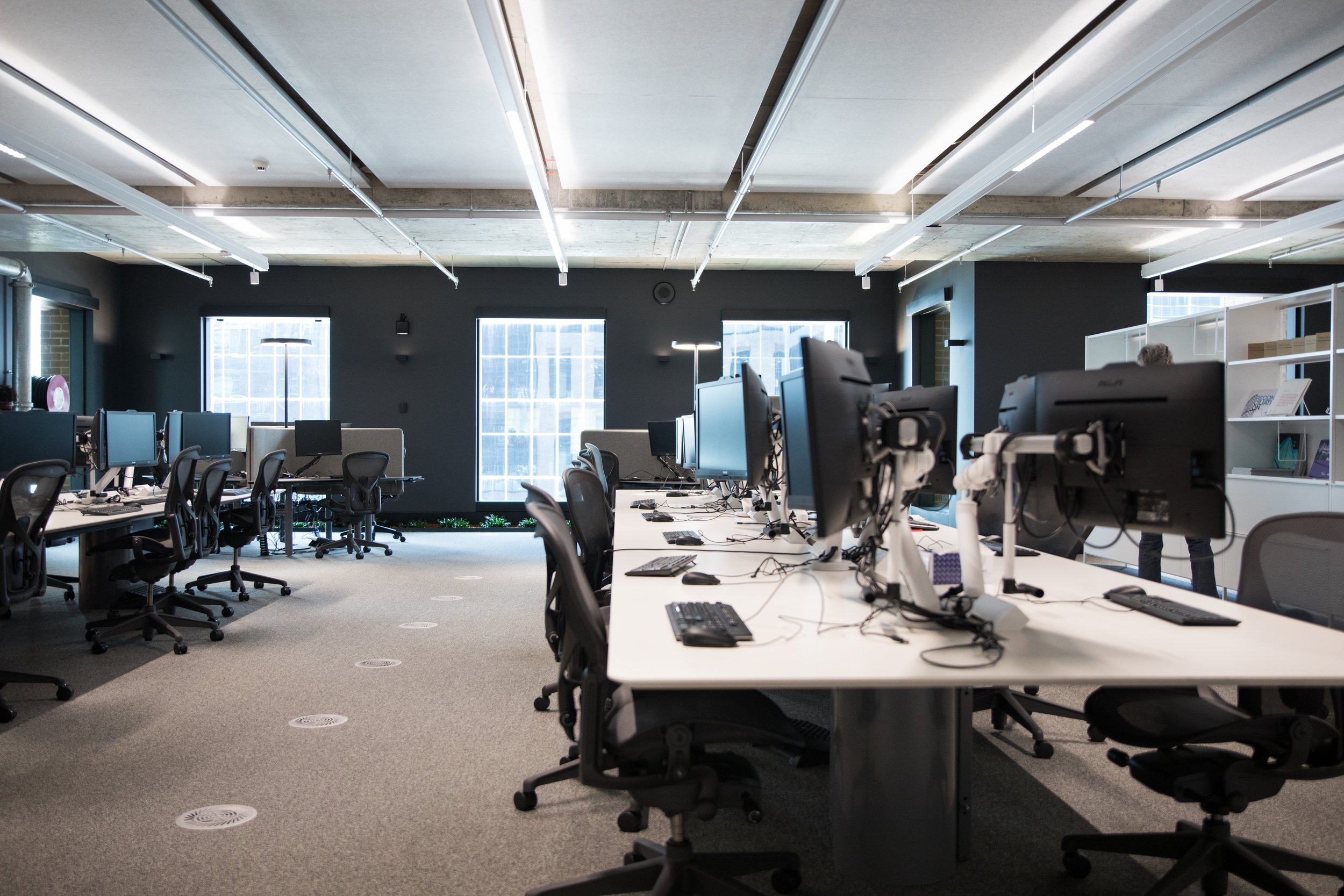 Oficina moderna con escritorios y computadoras, ventanas amplias y luz natural