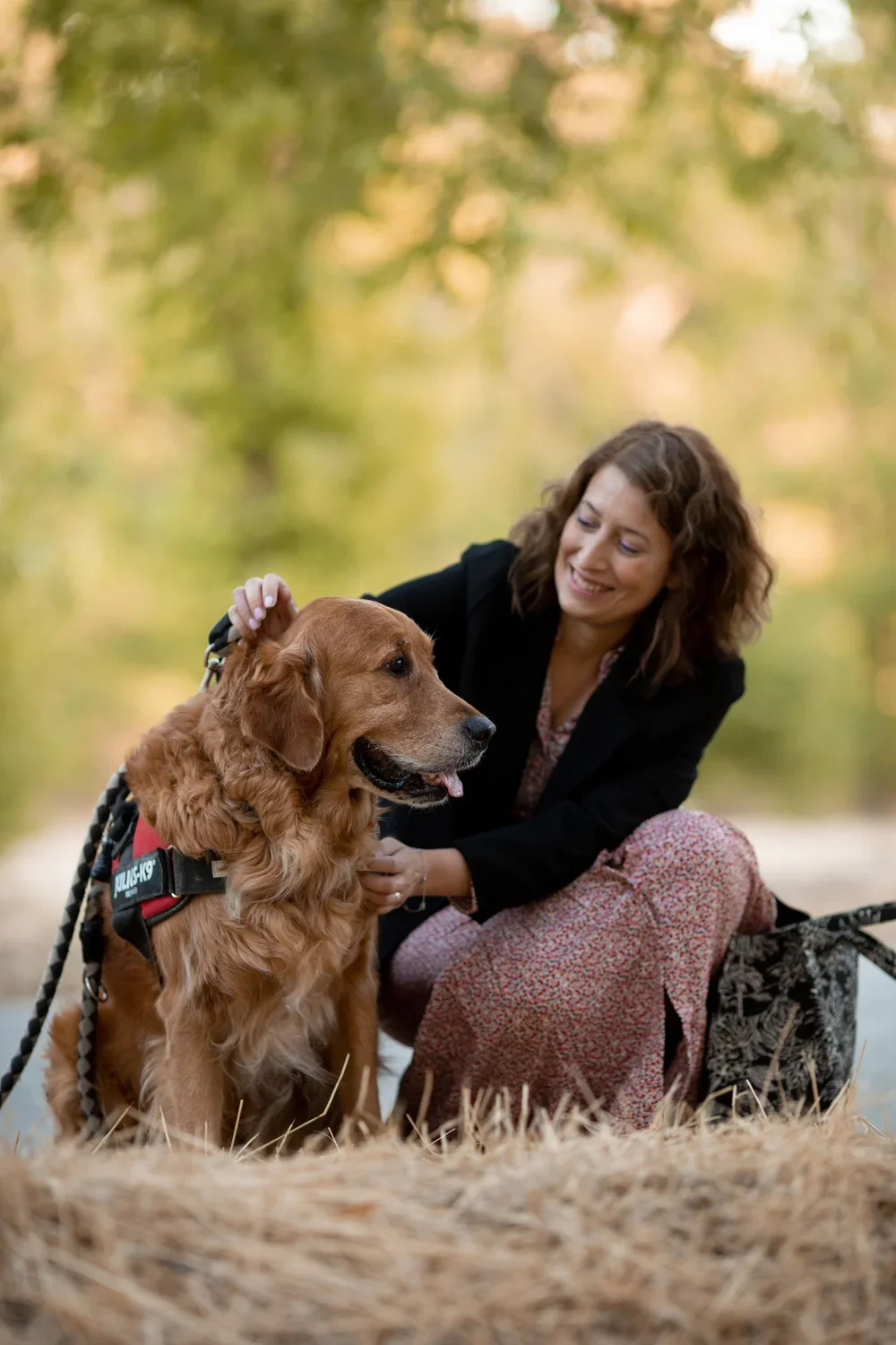 Una mujer sonriente acaricia a un perro golden retriever en un parque con fondo de árboles verdes.