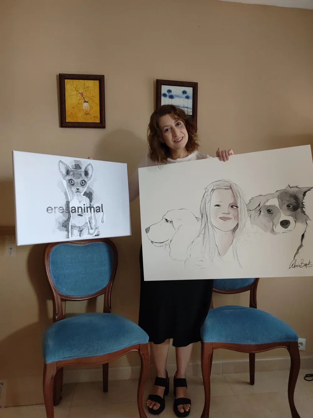 Mujer con cabello rizado sosteniendo una pintura de retrato de varios perros, y una cartulina con la palabra 'erejanimal' y un dibujo de un animal con cara de gato.