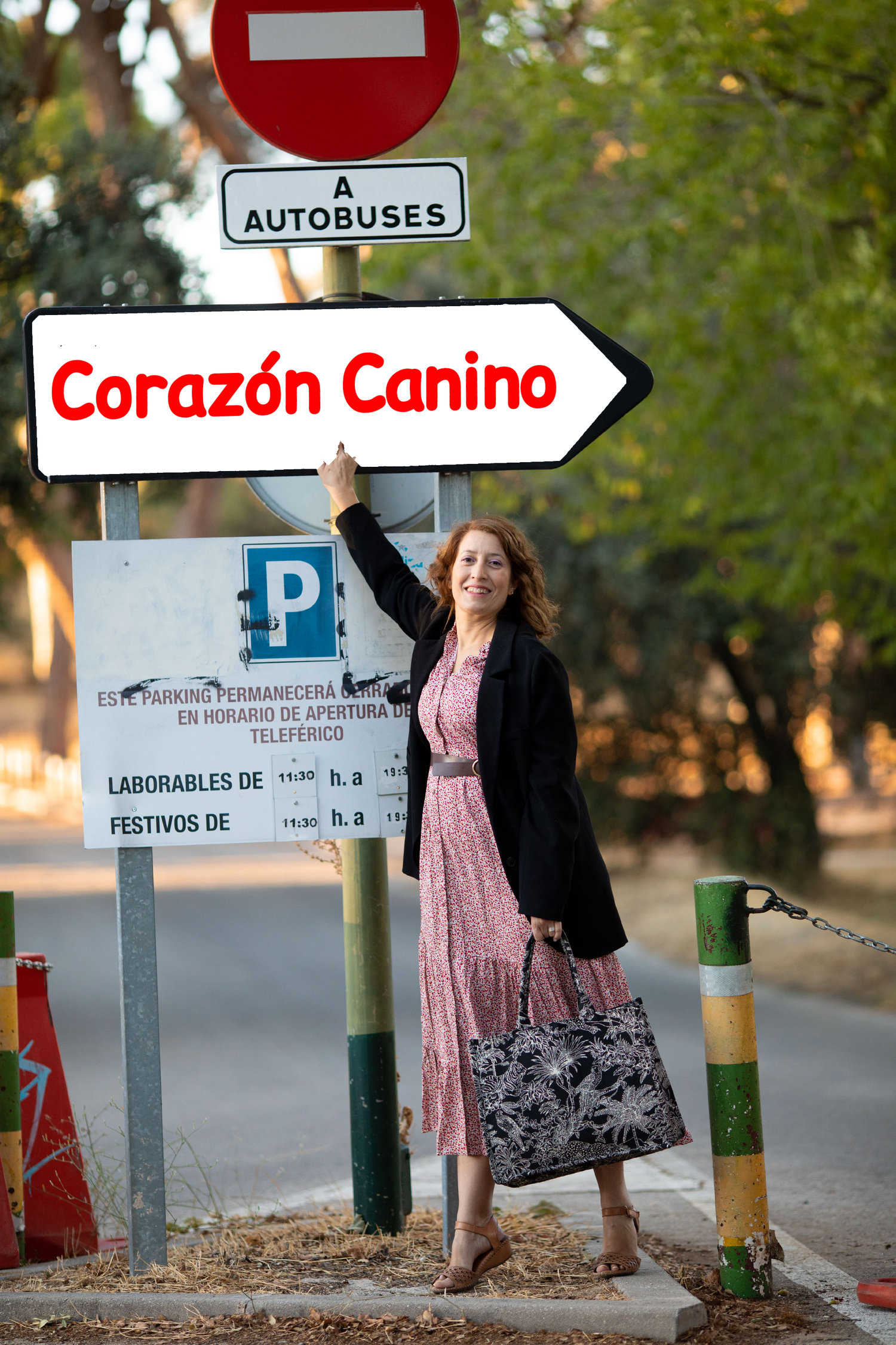 Señal de dirección con el texto 'Corazón Canino' y una mujer sonriendo señalando hacia la misma, en un entorno al aire libre.
