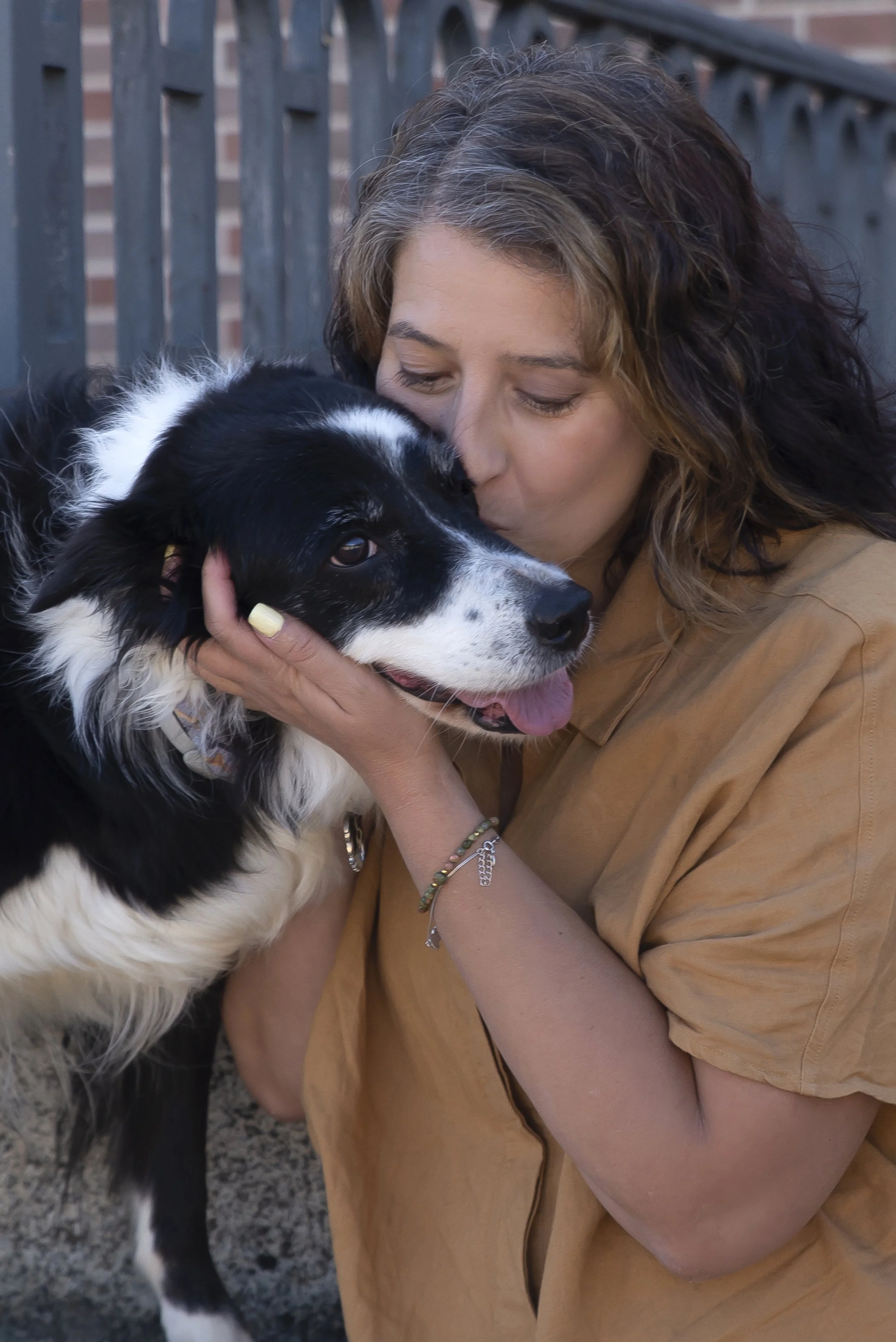 Una mujer está abrazando y besando a un perro Border Collie negro y blanco en un entorno exterior.