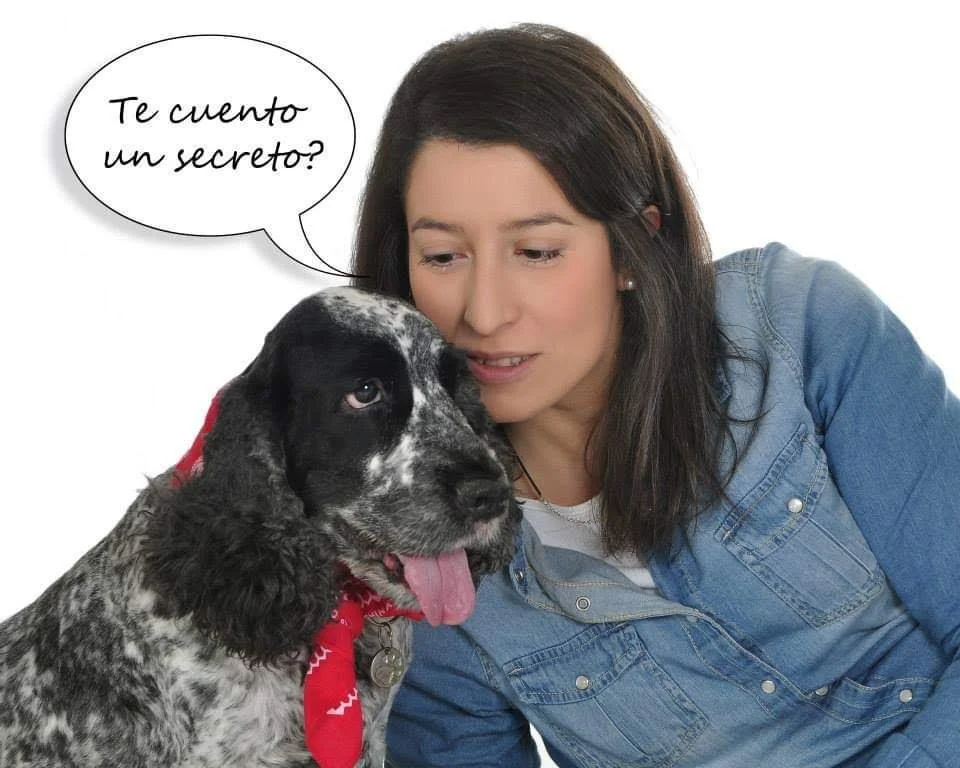 Una mujer y un perro con una bandana roja. La mujer le susurra al perro y hay un globo de diálogo que dice "¿Te cuento un secreto?"