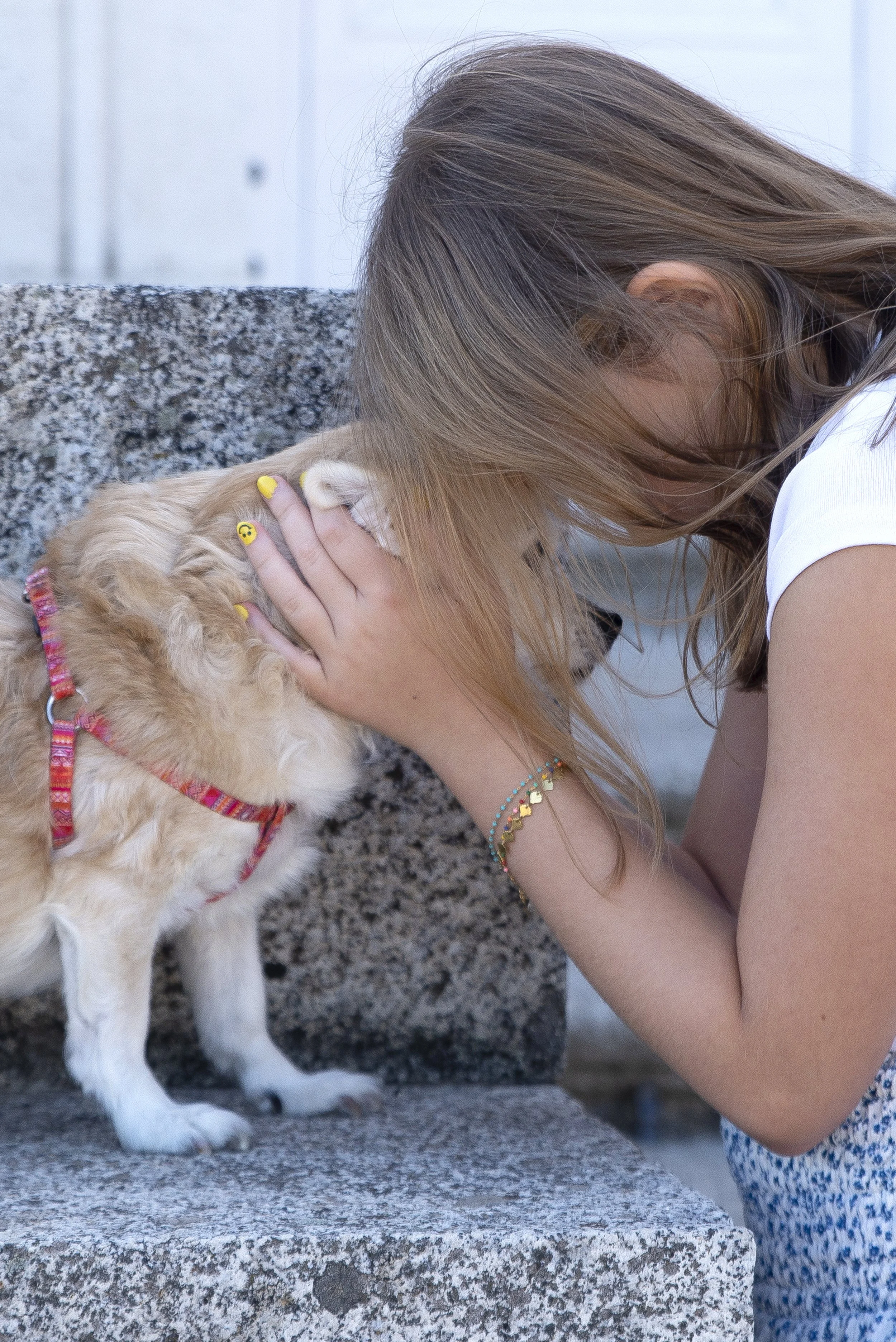 Una joven acaricia a un perro en la cara mientras ambos se miran fijamente, en un banco de piedra.