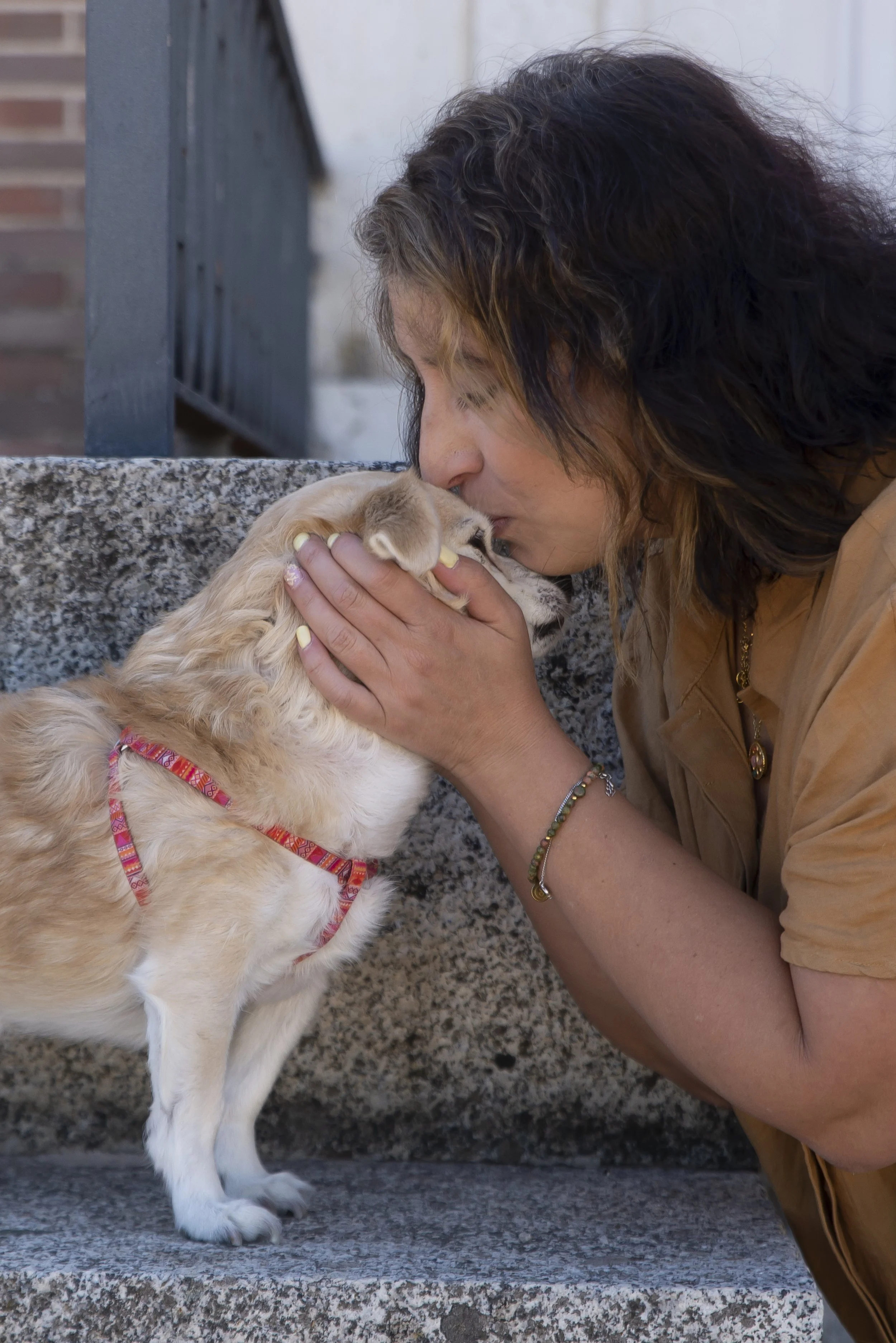 Mujer acariciando a un perro cachorro con cuerda de color rosa, en un lugar exterior de piedra.