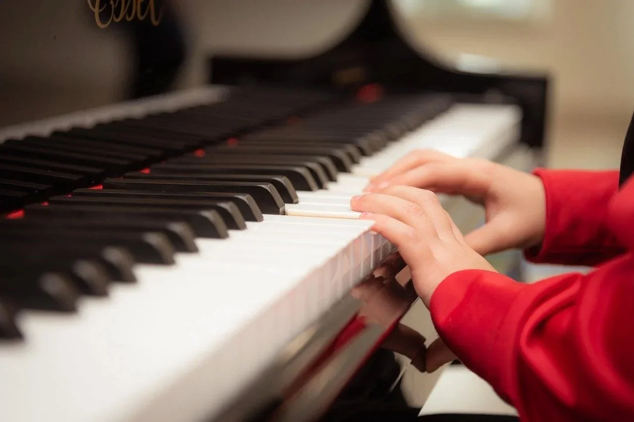 Main d'enfant jouant du piano, portant un vêtement rouge.