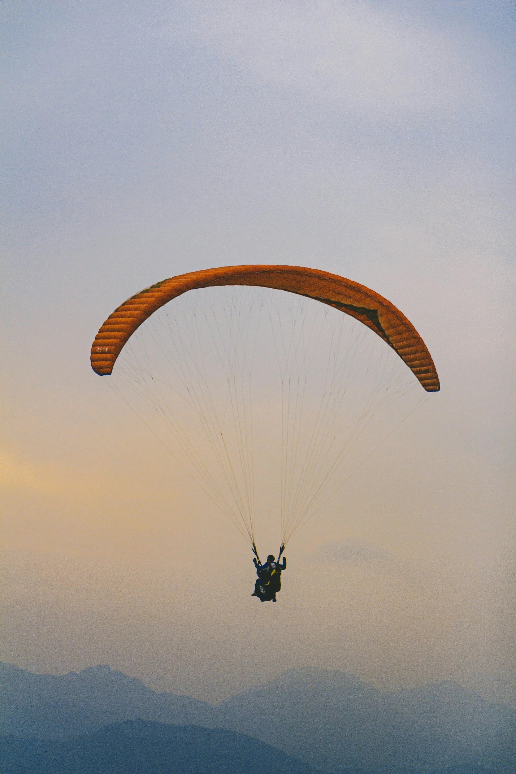 Ein Fallschirmspringer fliegt im Himmel bei Sonnenuntergang über Bergen, mit einem orangefarbenen Fallschirm in Afrika