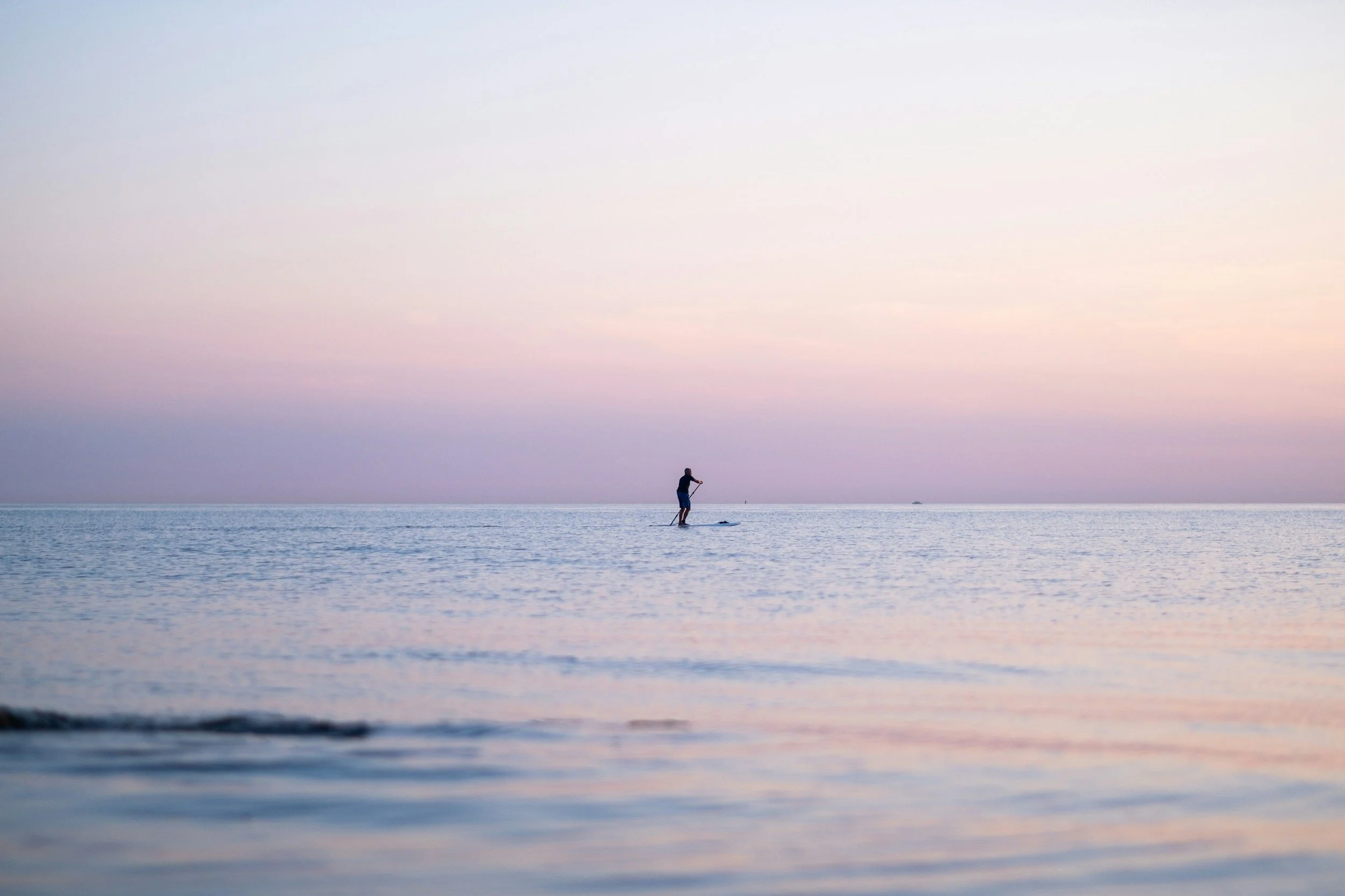 Ein Mann steht auf einem Stand-Up Paddle bei Sonnenuntergang im indischen Ozean in Afrika