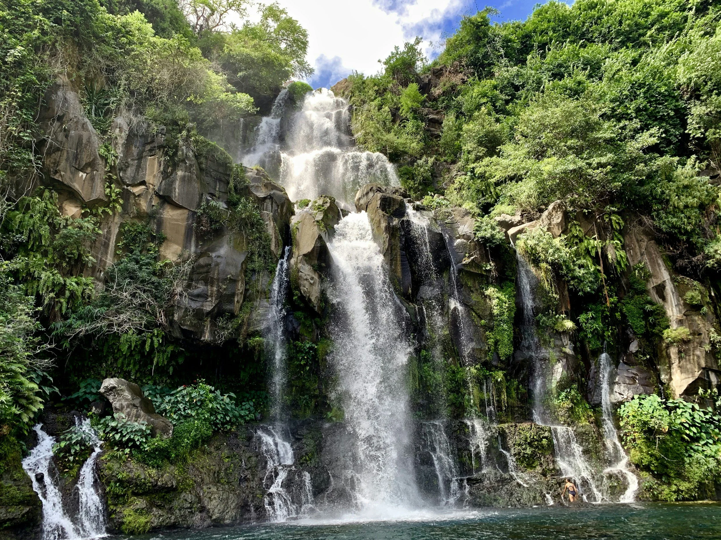 Bild eines Wasserfalls auf der Insel La Réunion mit Bäumen und einem kleinen See, in dem man schwimmen kann