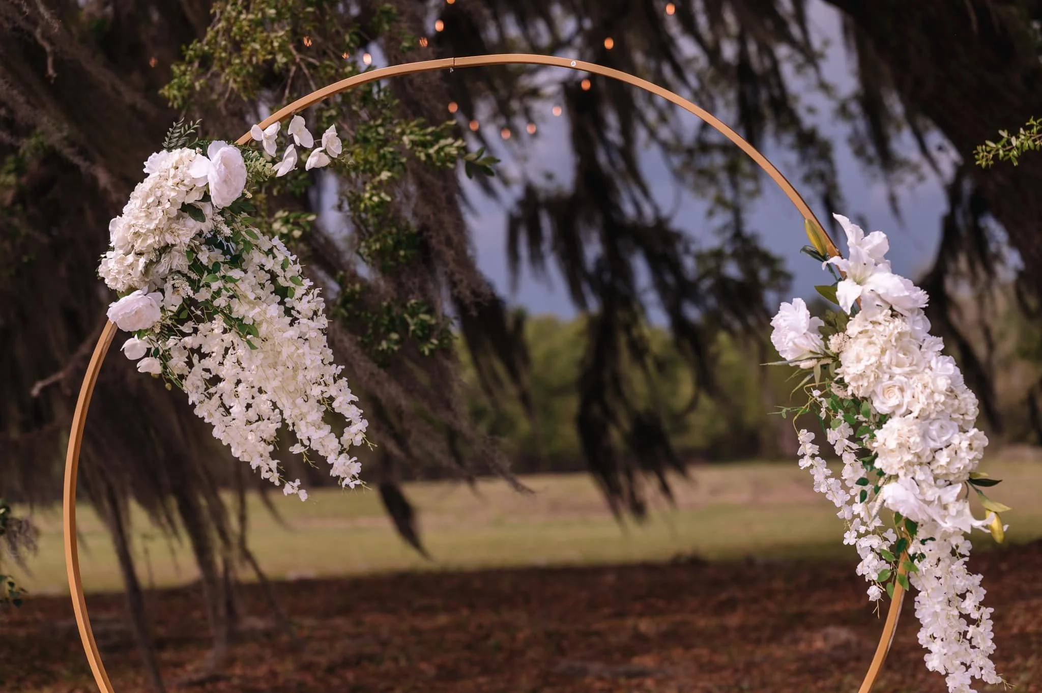 Floral wedding ceremony arch with oak tree background.