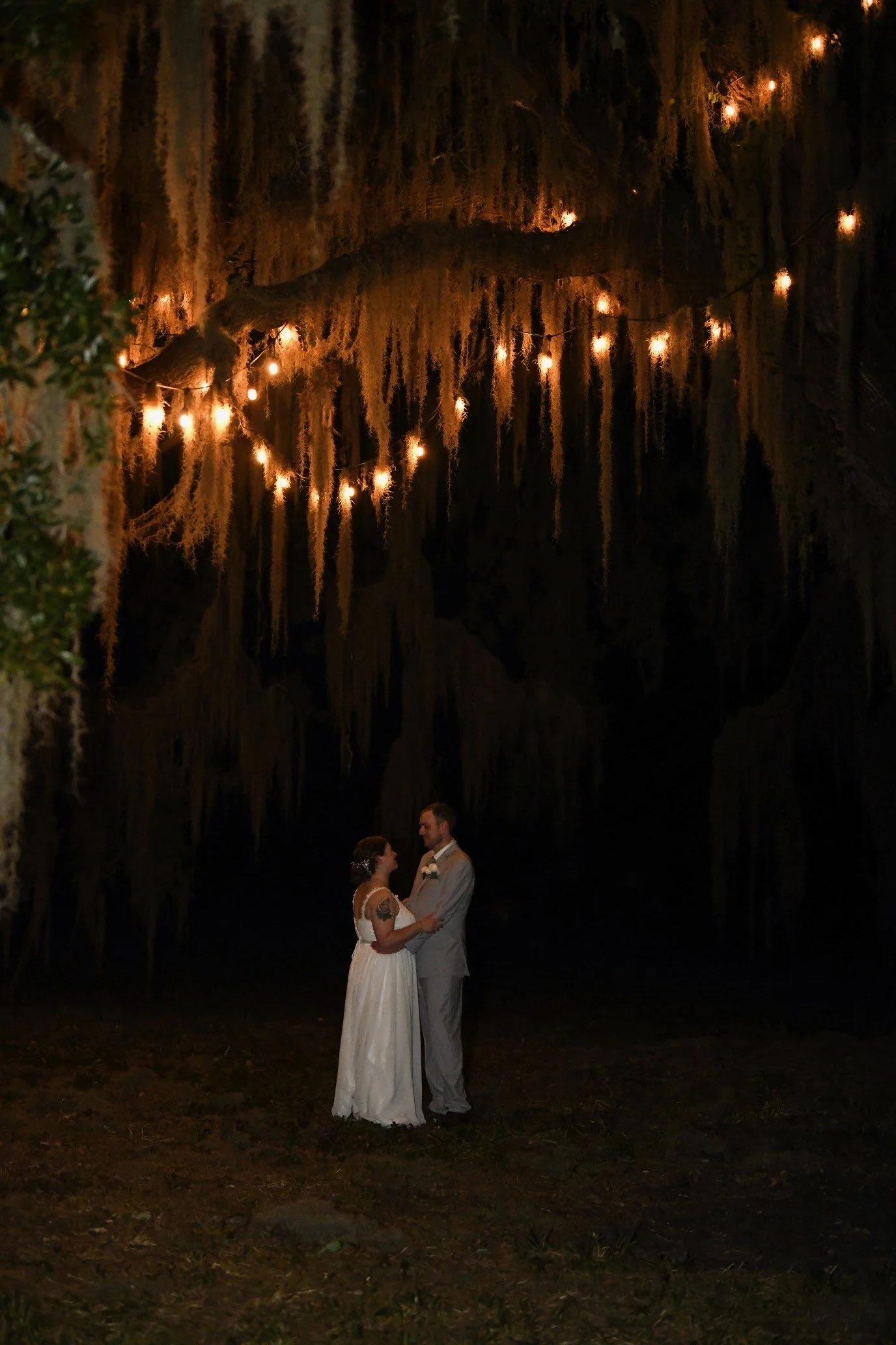 Bride and groom dance under the oak tree string lights.