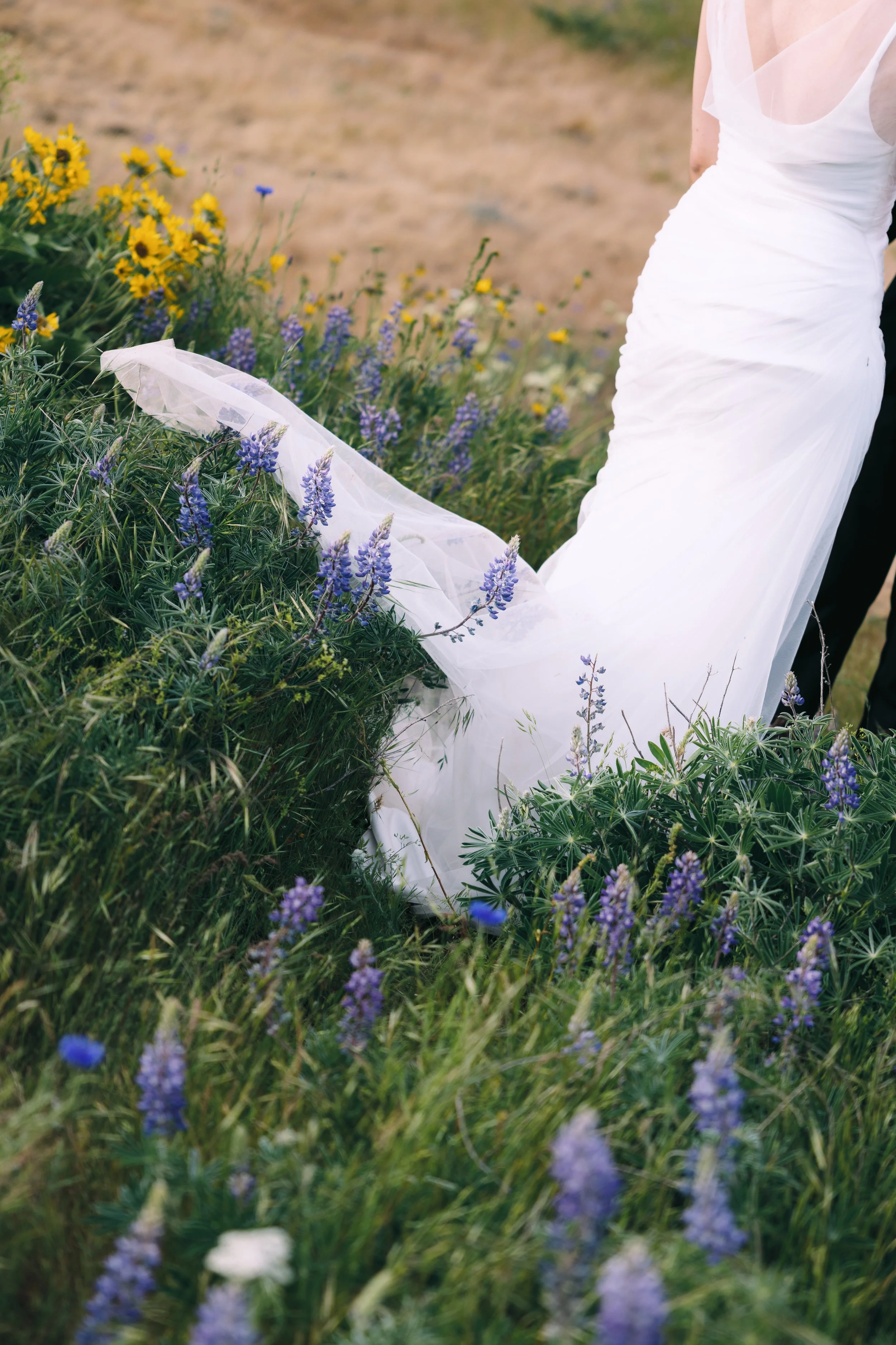 Close-up of a white dress moving through purple wildflowers during a spring engagement session.