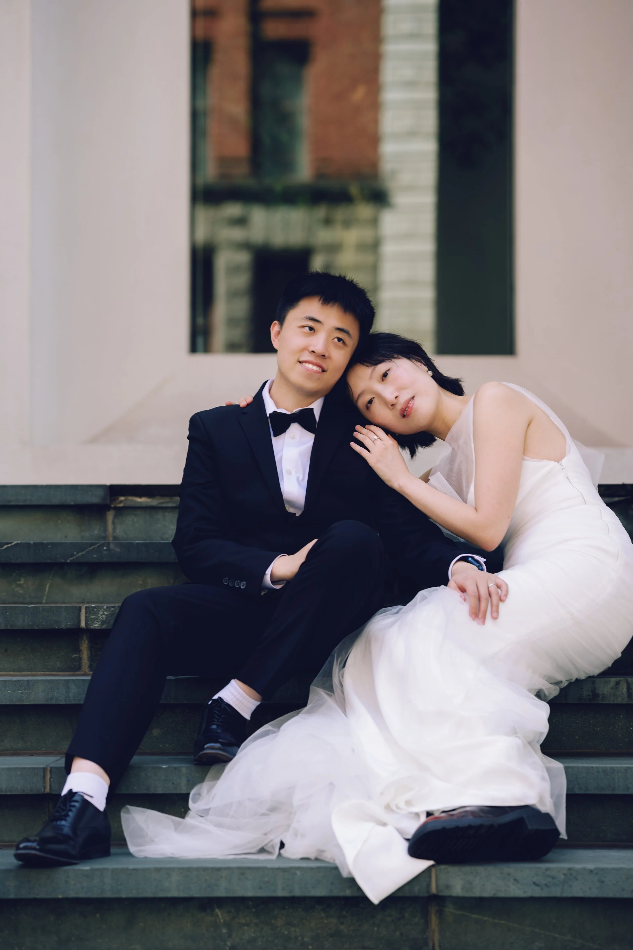 Engaged couple seated closely on steps, with the bride leaning gently on the groom’s shoulder.