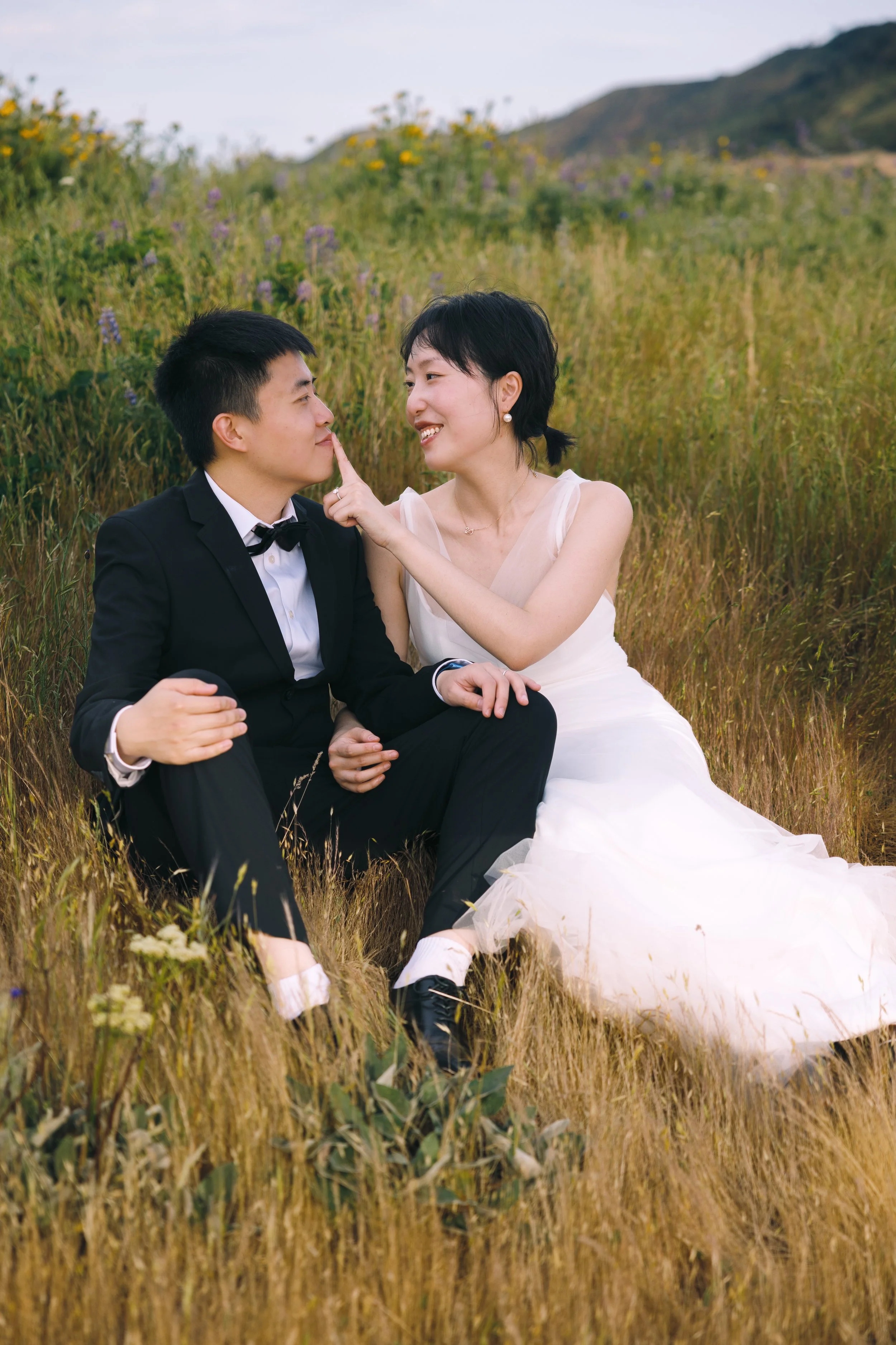 Engaged couple sitting together in tall grass and wildflowers at Tom McCall Preserve.